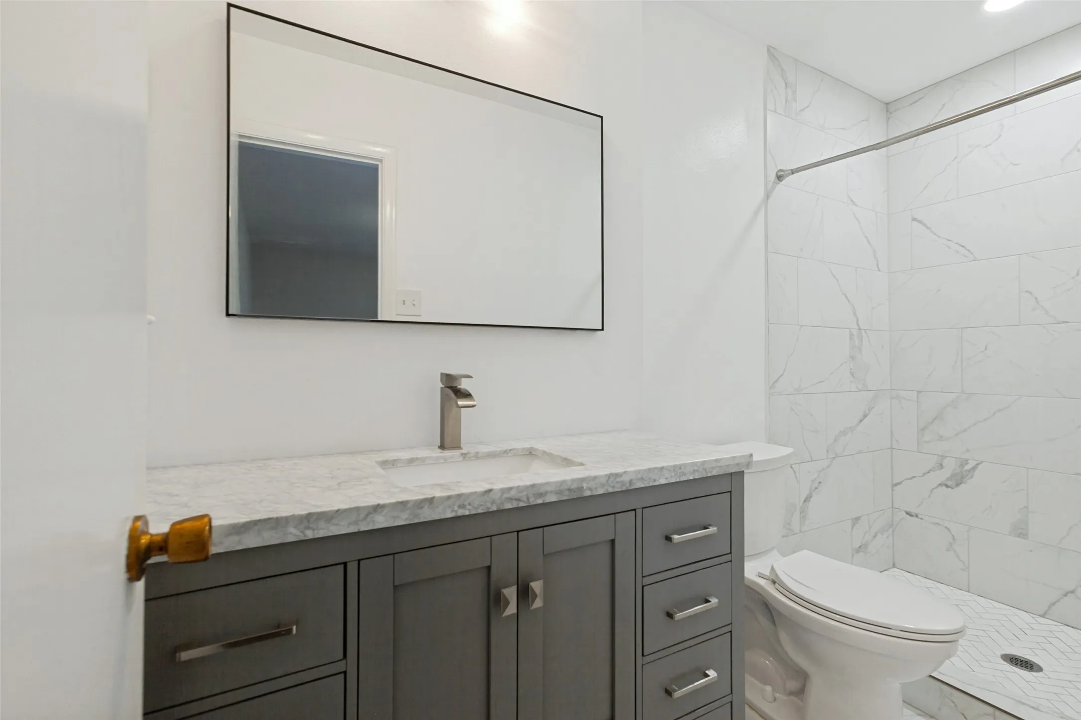 Modern vanity with a gray finish and integrated sink, stone countertop, brushed nickel faucet, and a black-framed mirror