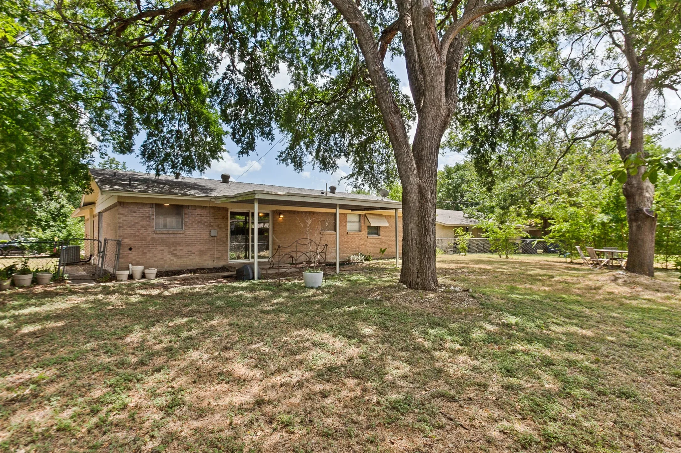 Spacious backyard featuring mature trees, a brick exterior, a covered patio, and large windows