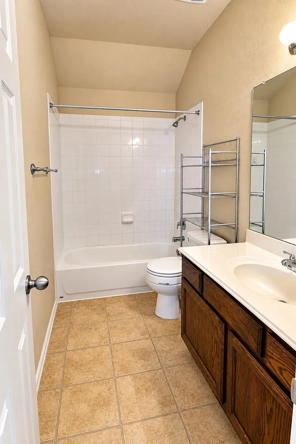 Ceramic tile flooring, white bathtub and shower with tile surround, wood-finish vanity with an integrated sink, and a framed mirror
