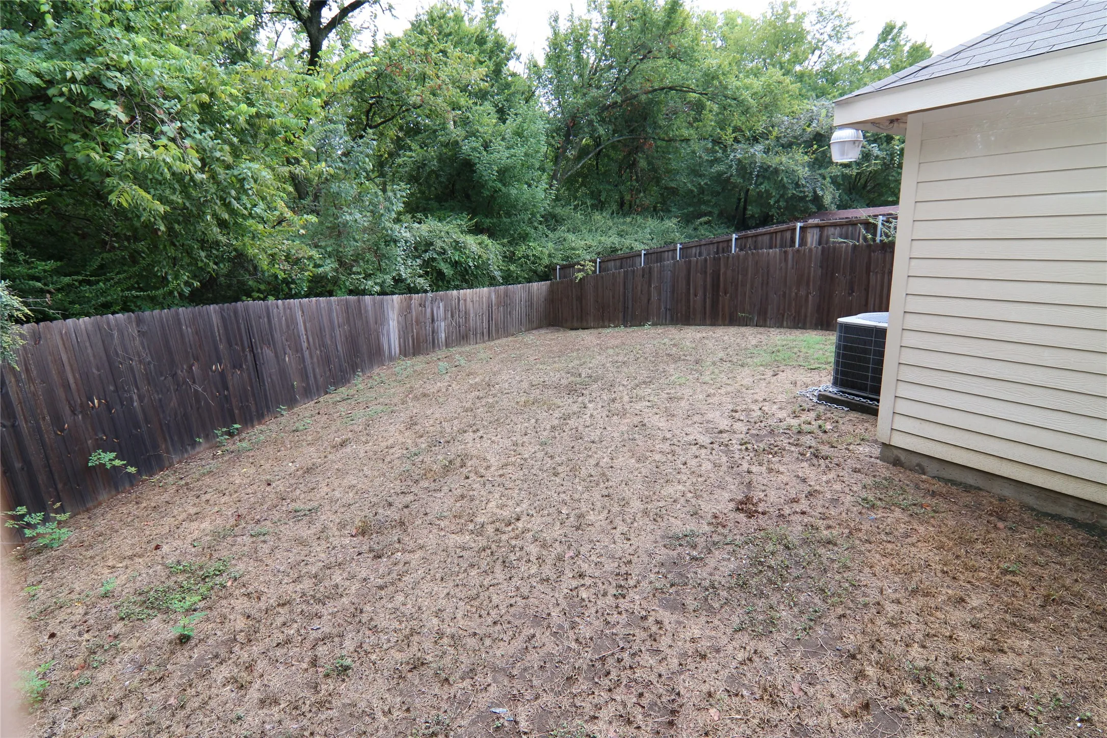 Expansive backyard with a full privacy fence, mature perimeter trees, and a visible exterior HVAC unit