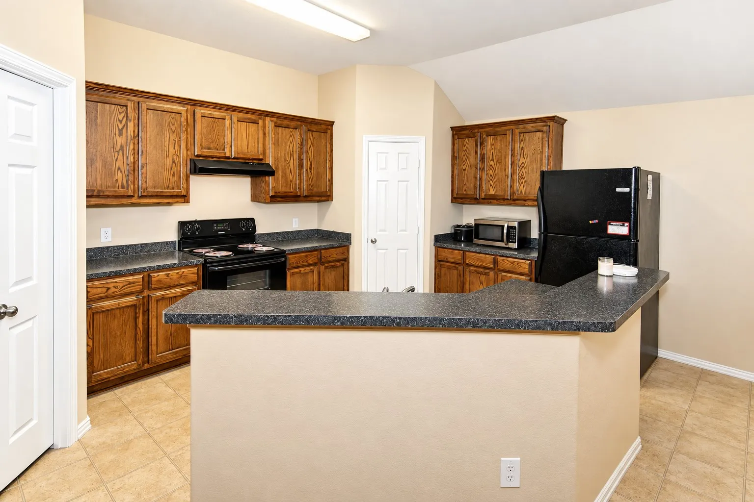 Kitchen featuring wood-finish cabinetry, dark countertops, built-in range, and tile flooring