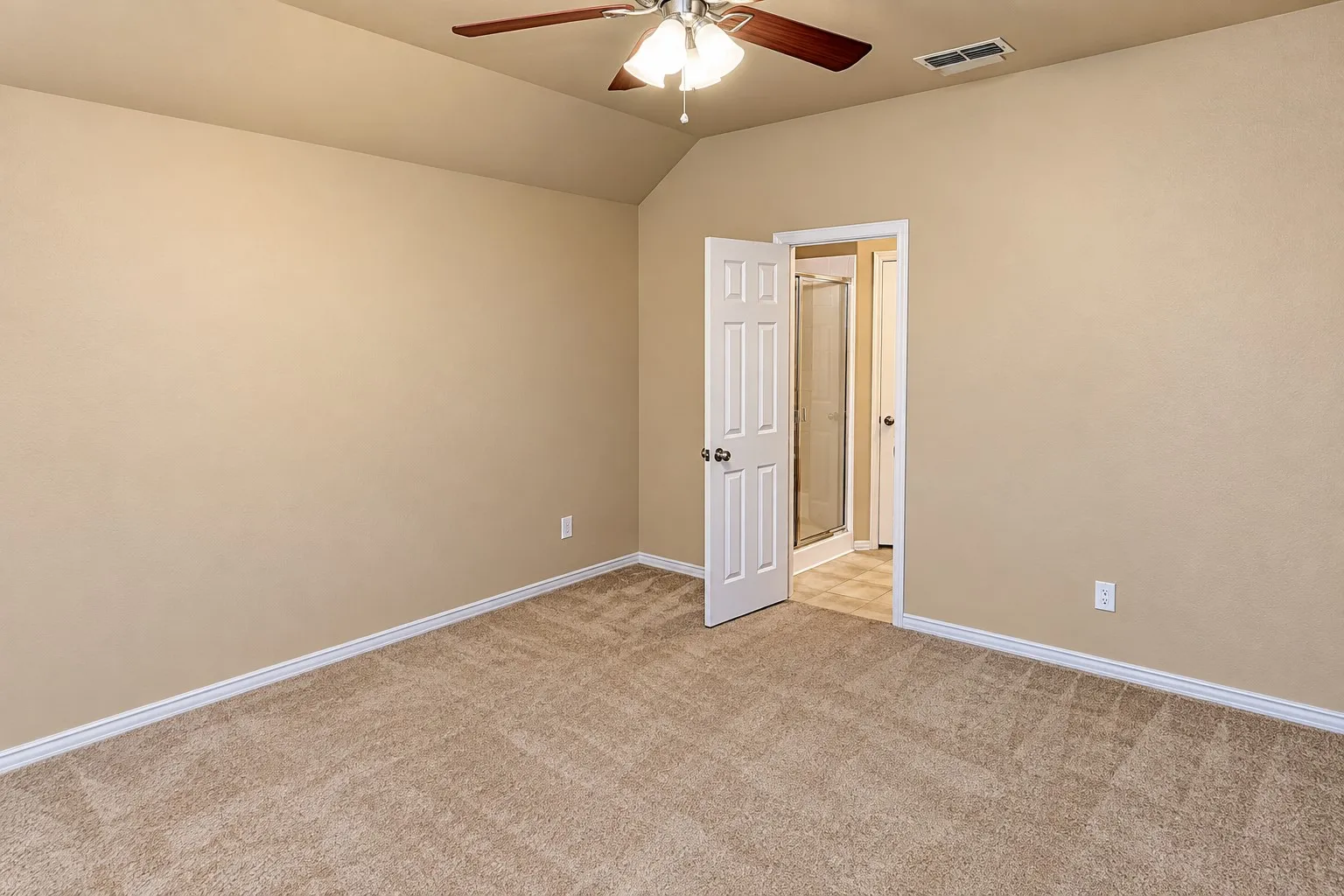 Vaulted ceiling with a ceiling fan, plush carpeting, paneled interior door, and an adjoining bathroom featuring a shower stall