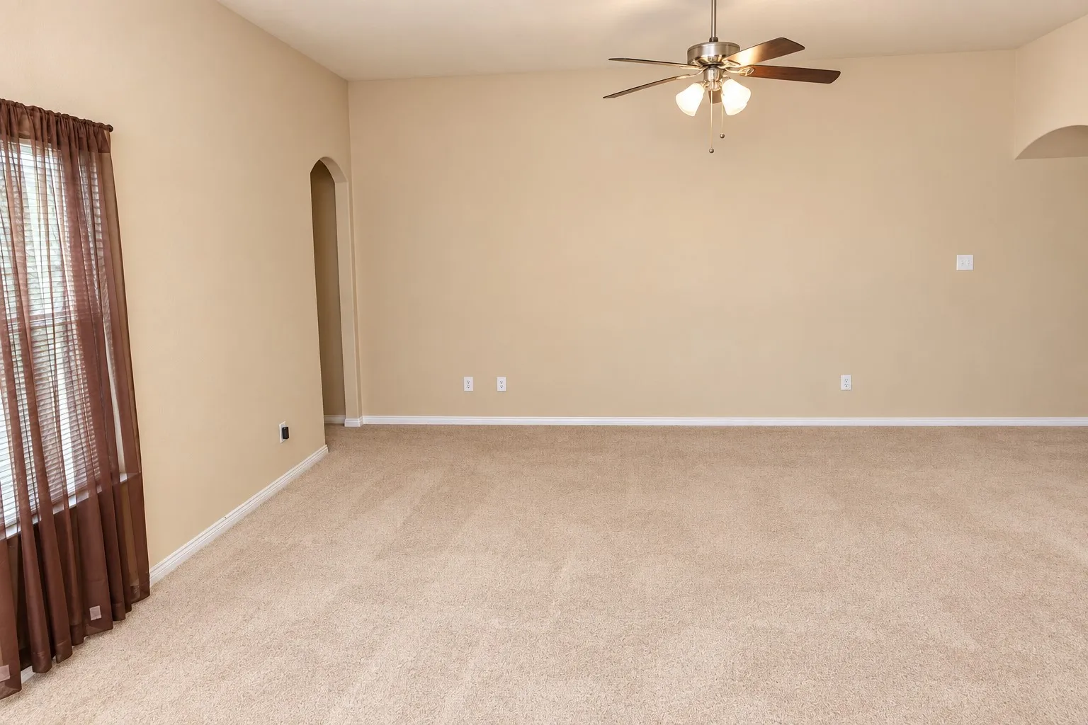Carpeted flooring, ceiling fan, natural light from window, arched doorway, and neutral wall paint