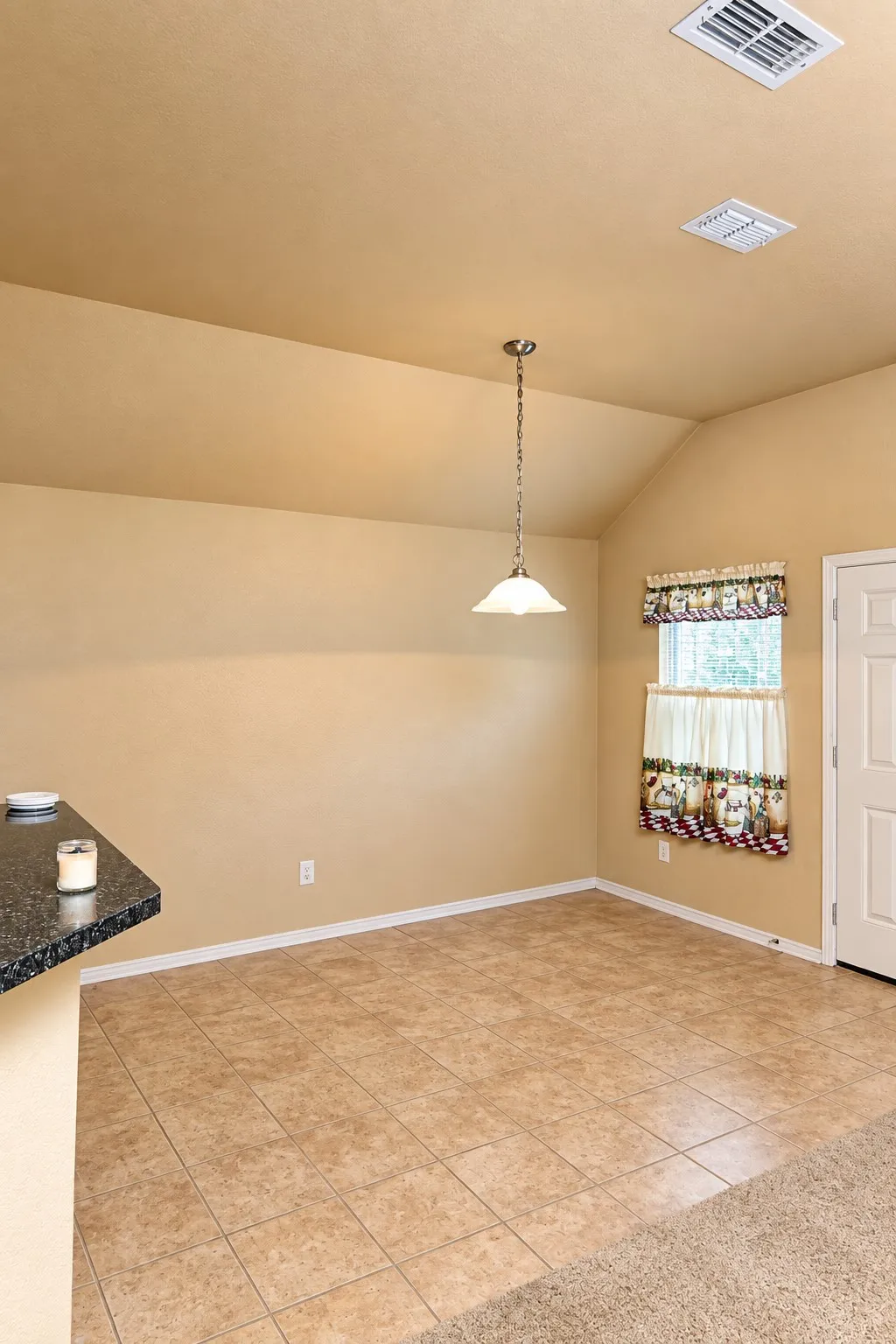 Vaulted ceiling with a pendant light fixture, tile flooring, and a window with trim