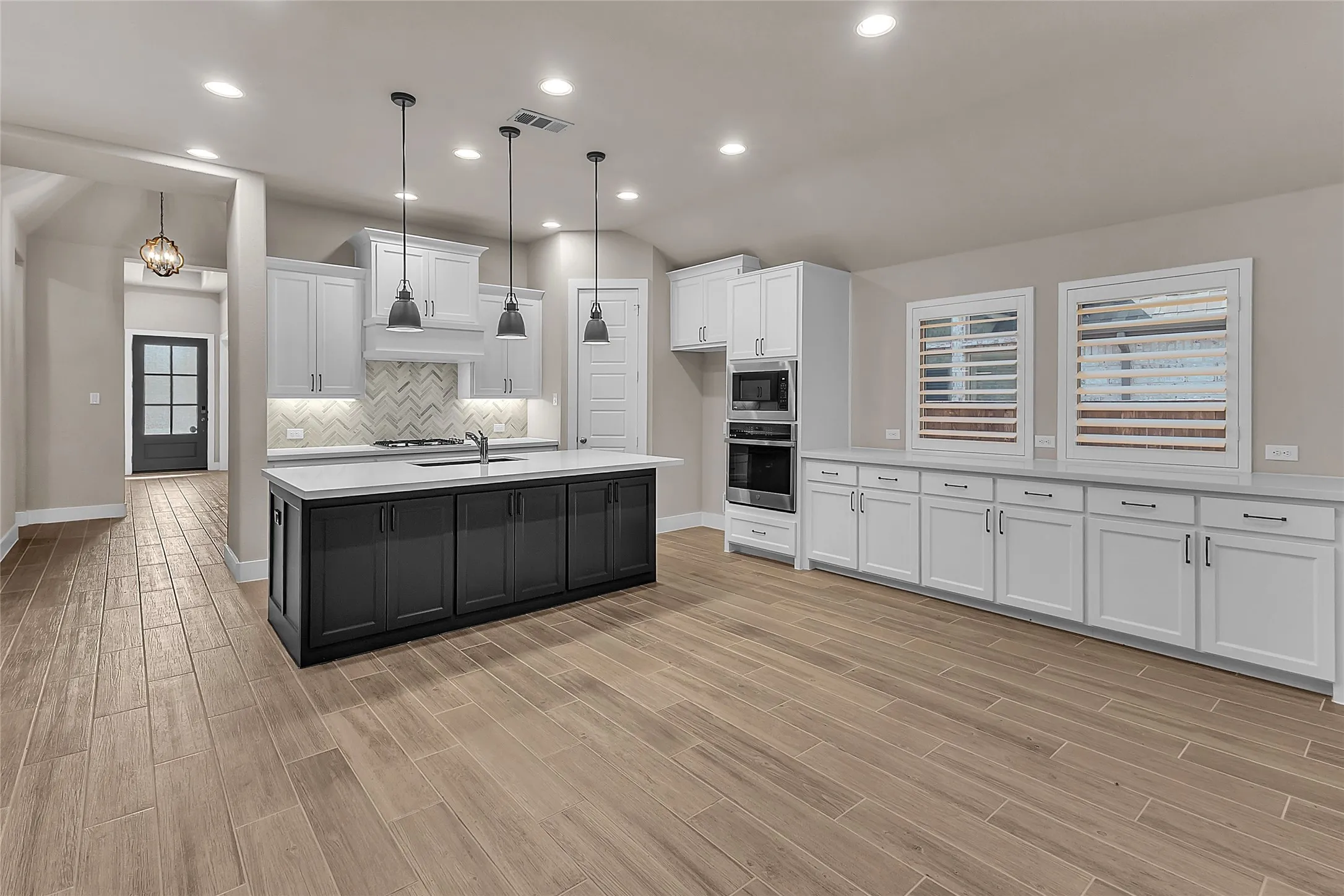 Open-plan kitchen with white and black cabinetry, quartz countertops, stainless steel appliances, herringbone backsplash, and recessed lighting.