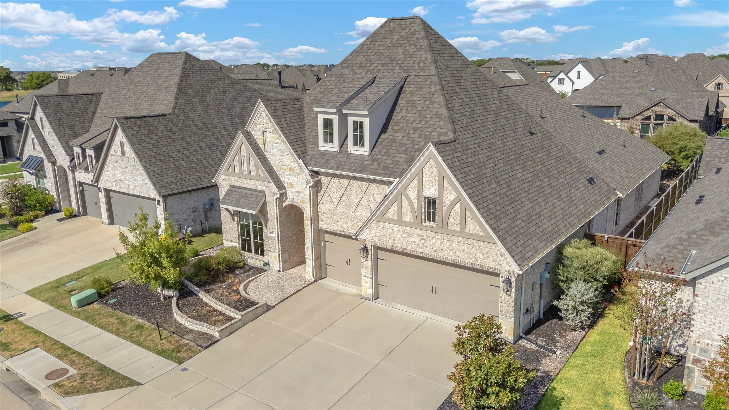 Three-car garage with smooth concrete driveway, stone and brick exterior finishes, gable rooflines, and well-maintained landscaping.