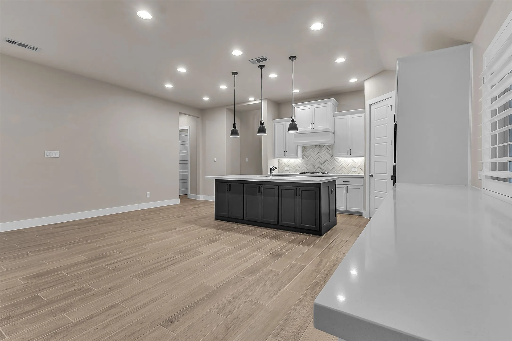 Open-plan kitchen with black island, white cabinetry, quartz countertops, and recessed lighting, highlighted by a herringbone tile backsplash and hardwood floors