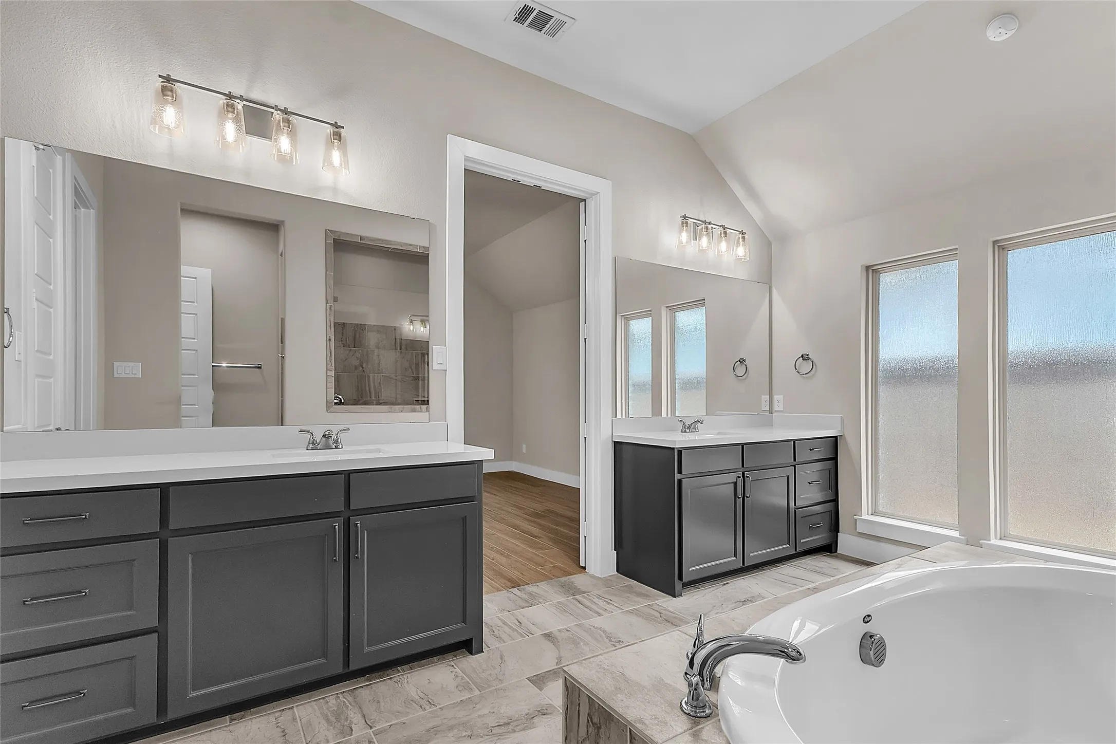 Primary bathroom with dual sinks, quartz countertops, large wall mirrors, and natural light from two windows in a bright open layout.