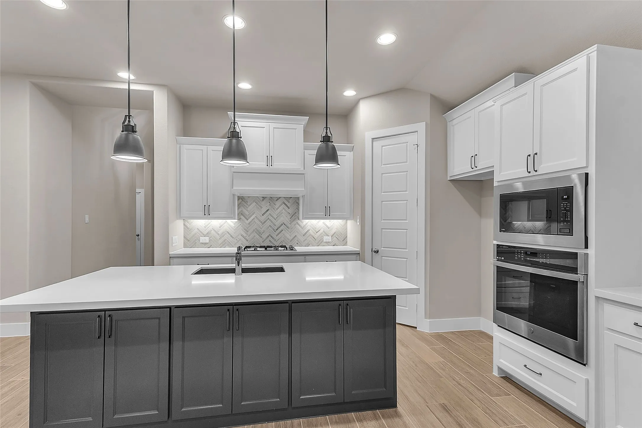 Open-plan kitchen with white cabinetry, stainless steel appliances, quartz countertops, herringbone tile backsplash, and recessed lighting
