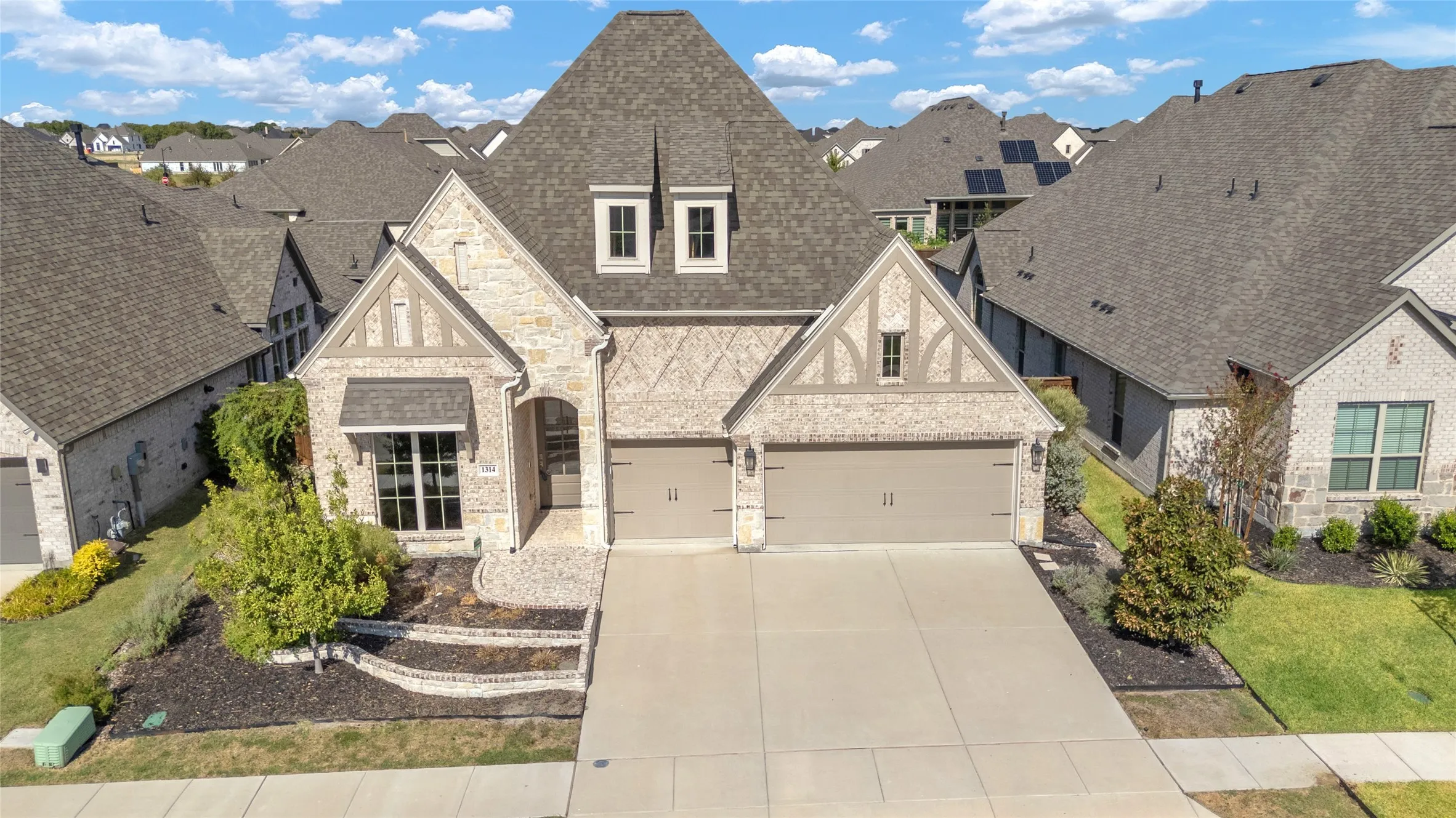 Three-car garage with stone and brick exterior, concrete driveway, and landscaped front yard with shrubs and ornamental trees