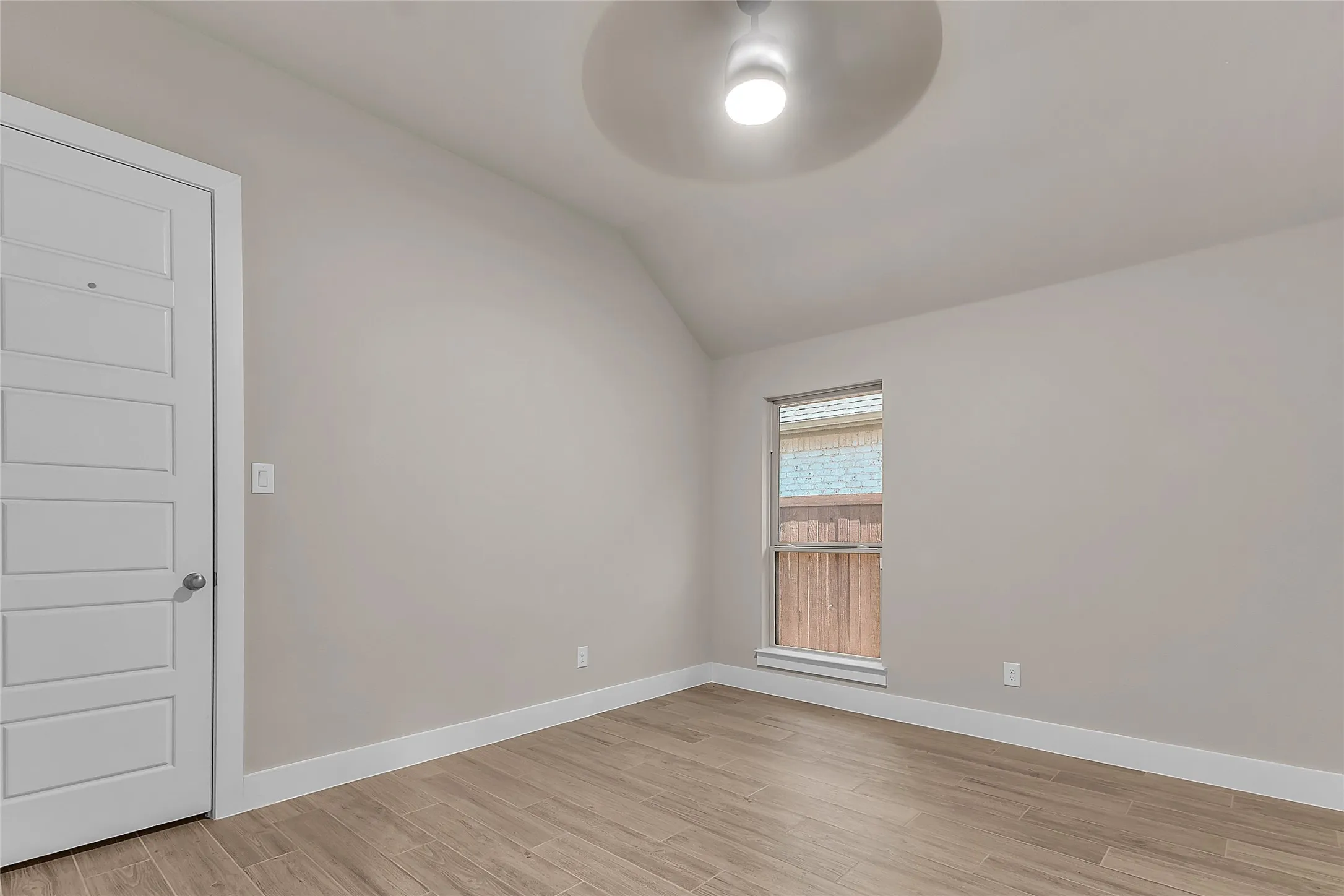 Bedroom with vaulted ceiling, large window, and hardwood flooring. Natural light enhances the minimalist design and neutral color palette.