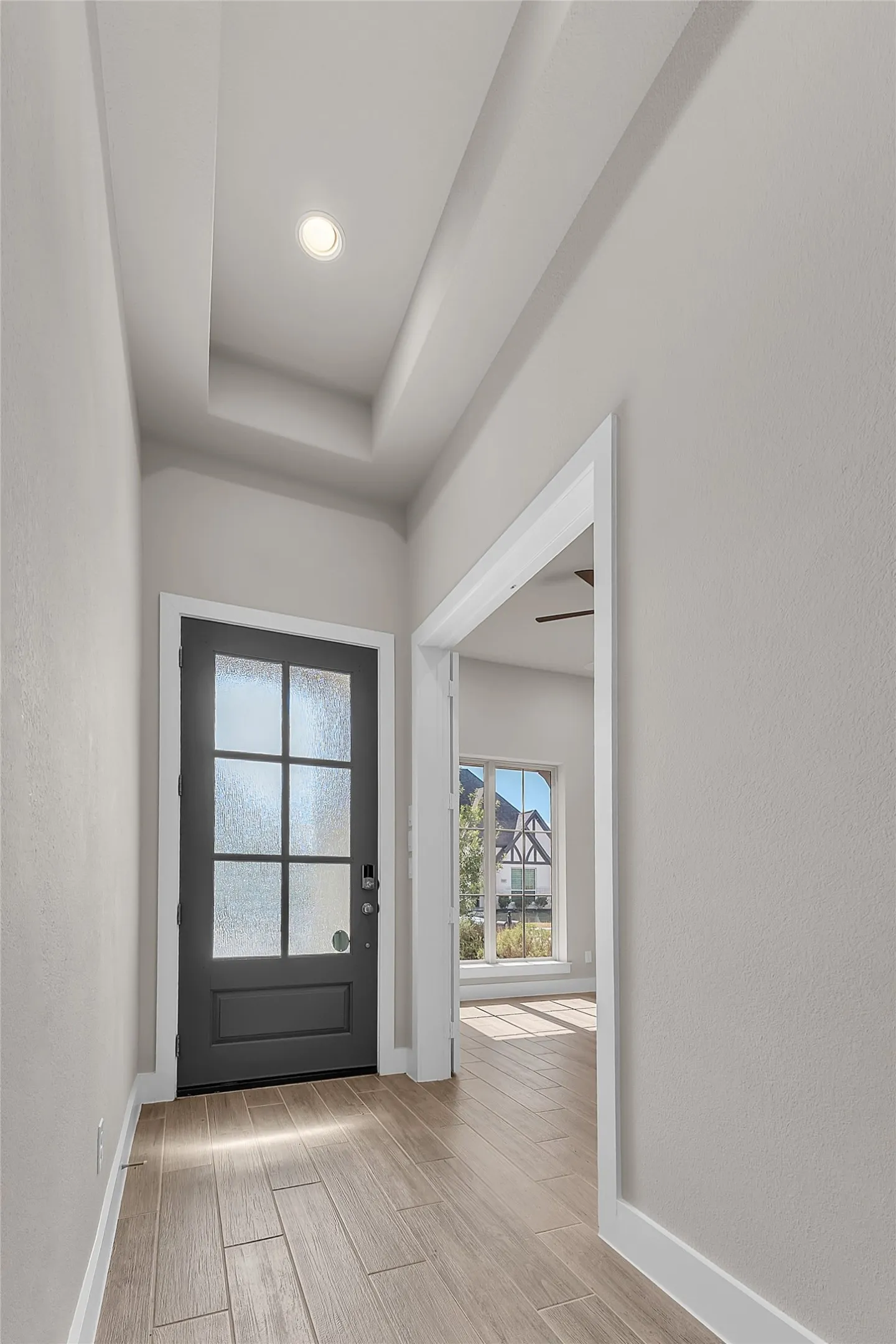 Entryway with a modern black front door, textured glass, and natural light flowing through a side window, showcasing neutral walls and tile flooring.