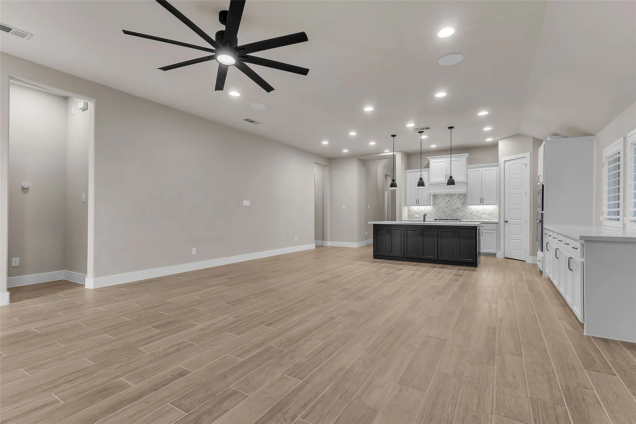 Open-plan living area with hardwood flooring, recessed lighting, and a central kitchen island topped with dark cabinetry and a light quartz countertop.