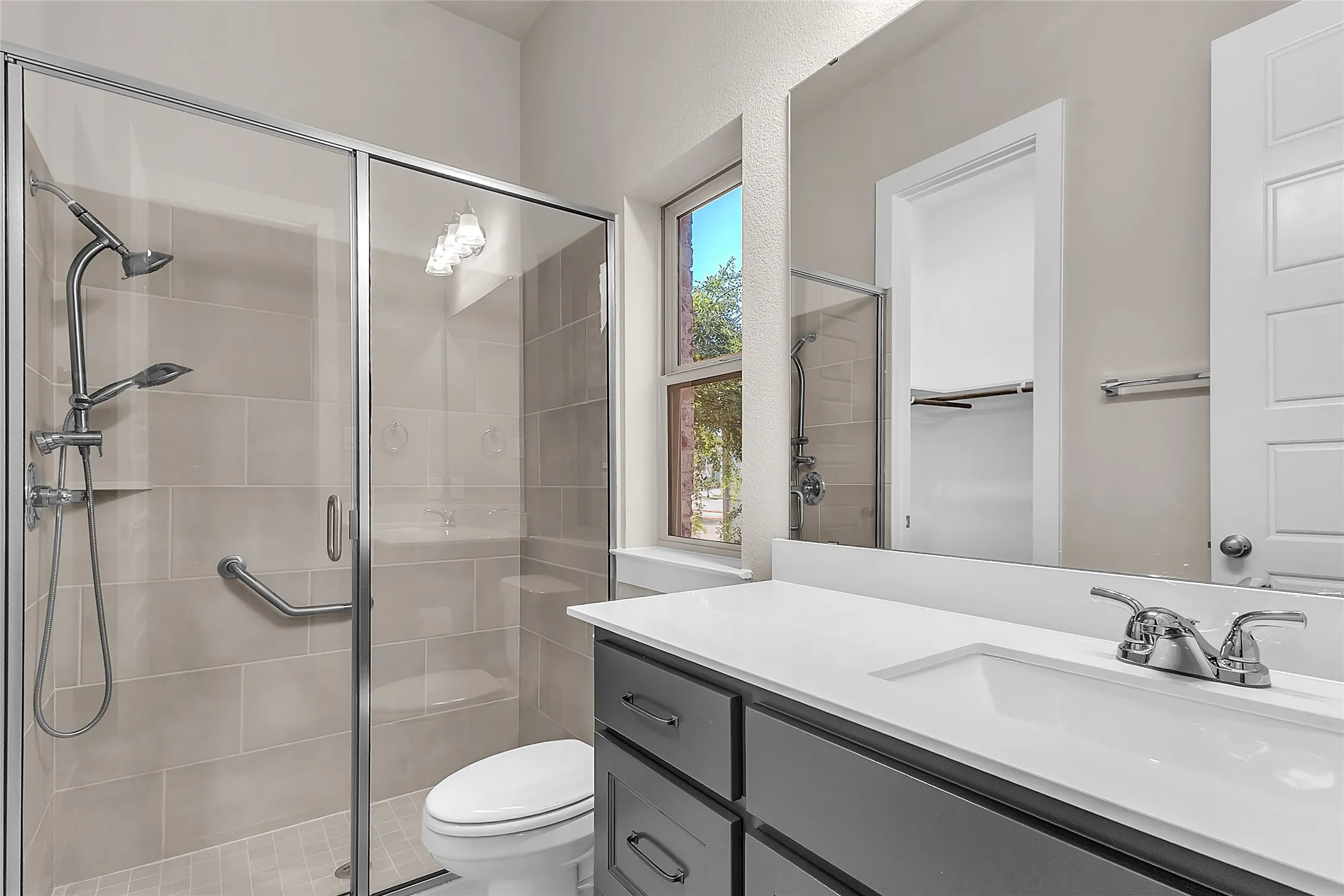Modern bathroom with glass shower enclosure, porcelain tiles, chrome fixtures, and natural light from a window highlighting the clean layout