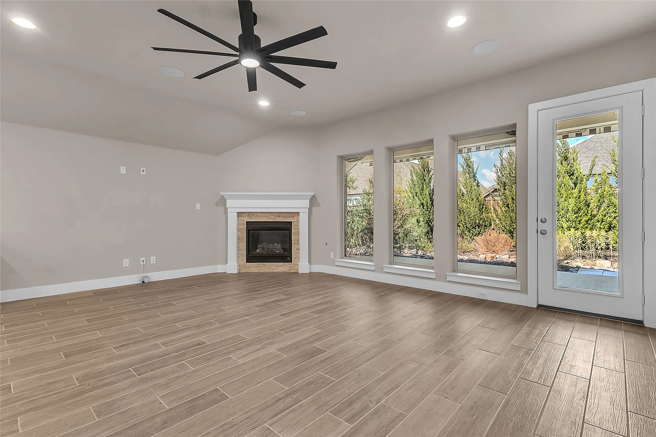 Living room with large windows, porcelain flooring, a modern ceiling fan, and a cozy fireplace, illuminated by natural light