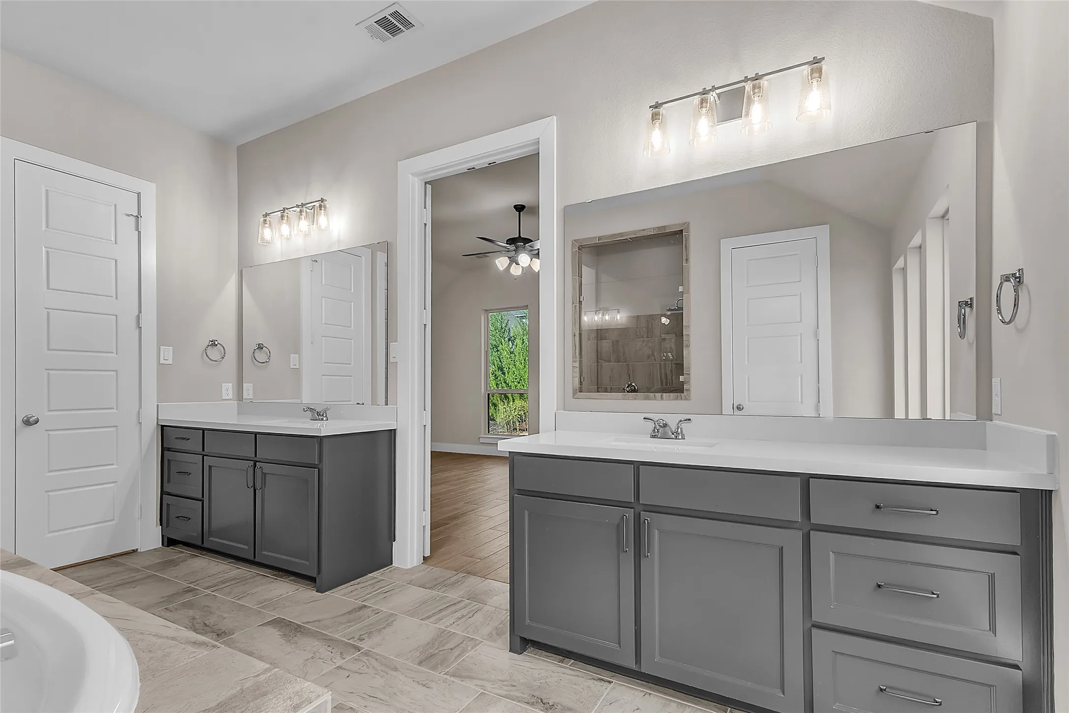 Master bathroom with dual vanities, quartz countertops, large mirrors, brushed nickel fixtures, and natural light from a nearby window.
