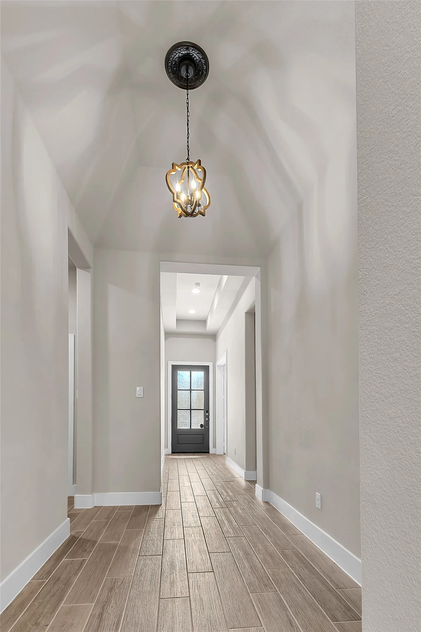Hallway with wood-look tile flooring, vaulted ceiling, and chandelier, leading to a front door with glass panels.