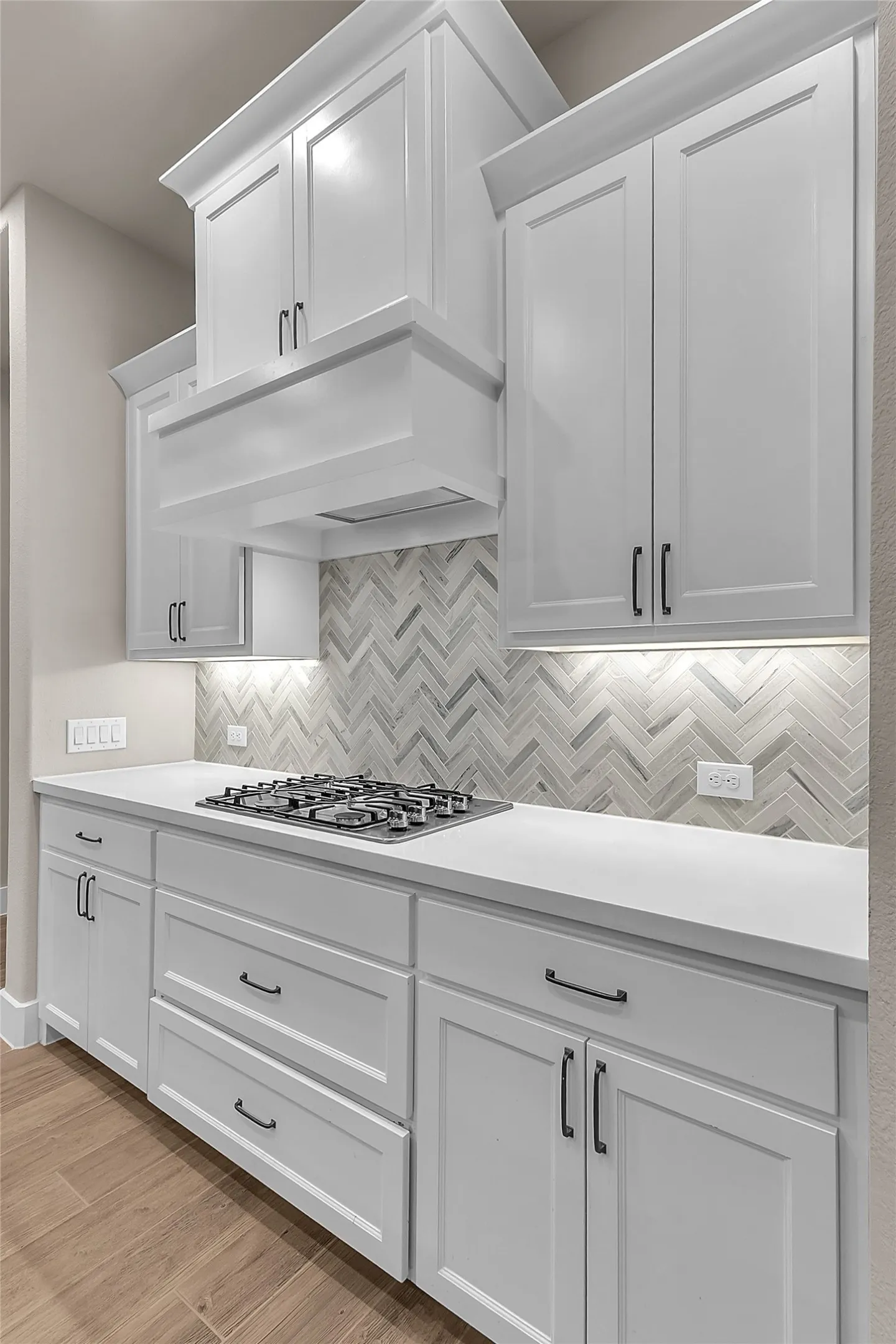 Open-plan kitchen with white cabinetry, quartz countertops, herringbone backsplash, stainless steel appliances, and under-cabinet lighting