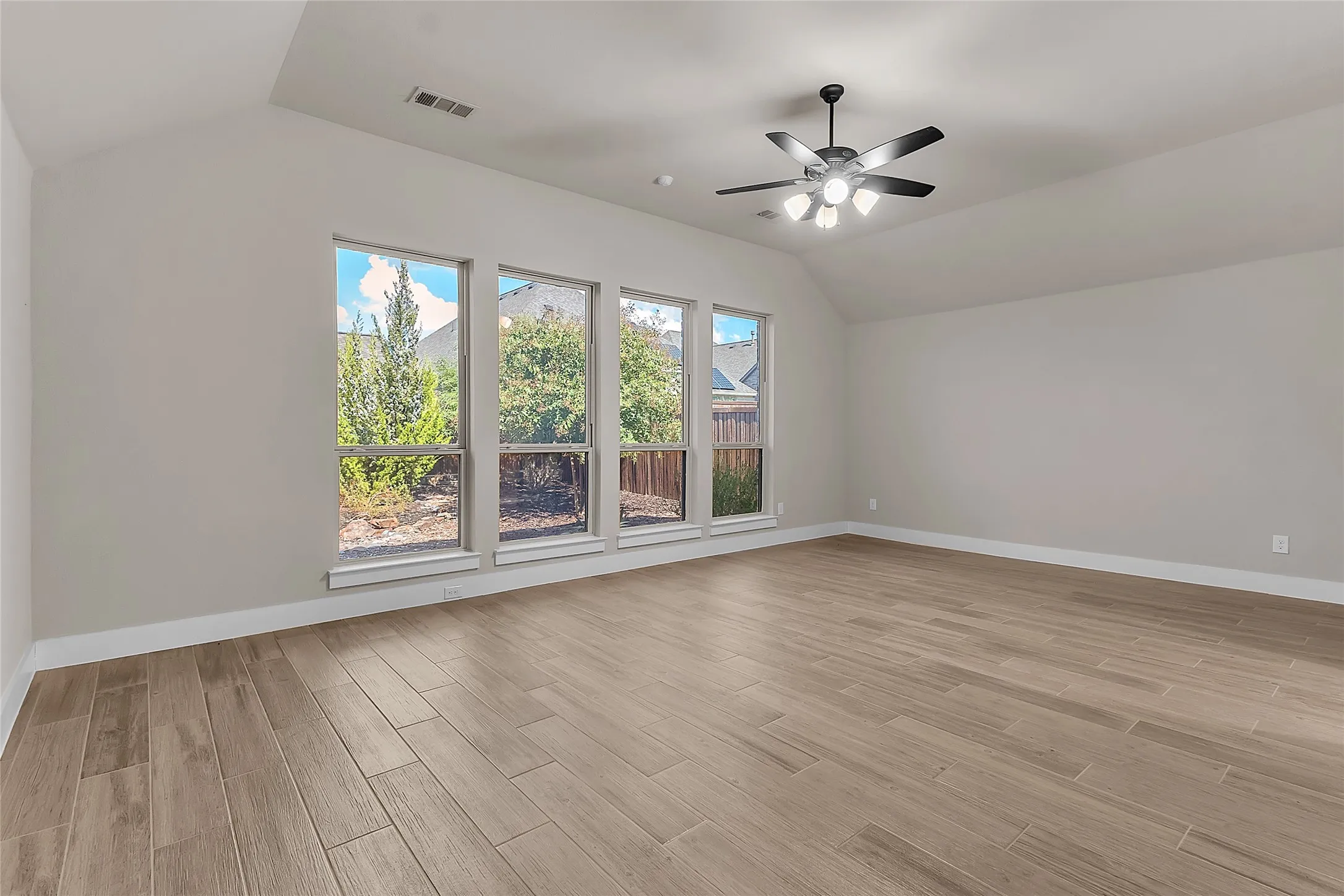 Living room with large floor-to-ceiling windows, hardwood-like tile flooring, and a vaulted ceiling providing abundant natural light.