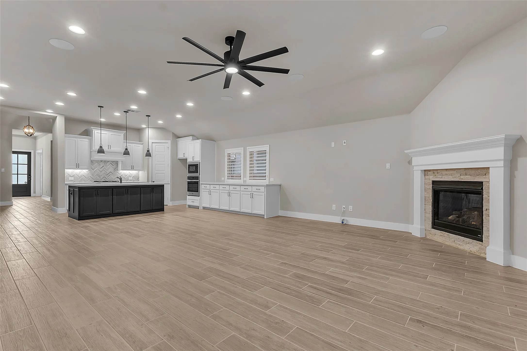 Open-plan living area with hardwood floors, quartz kitchen island, recessed lighting, and a modern ceiling fan adjacent to a cozy fireplace