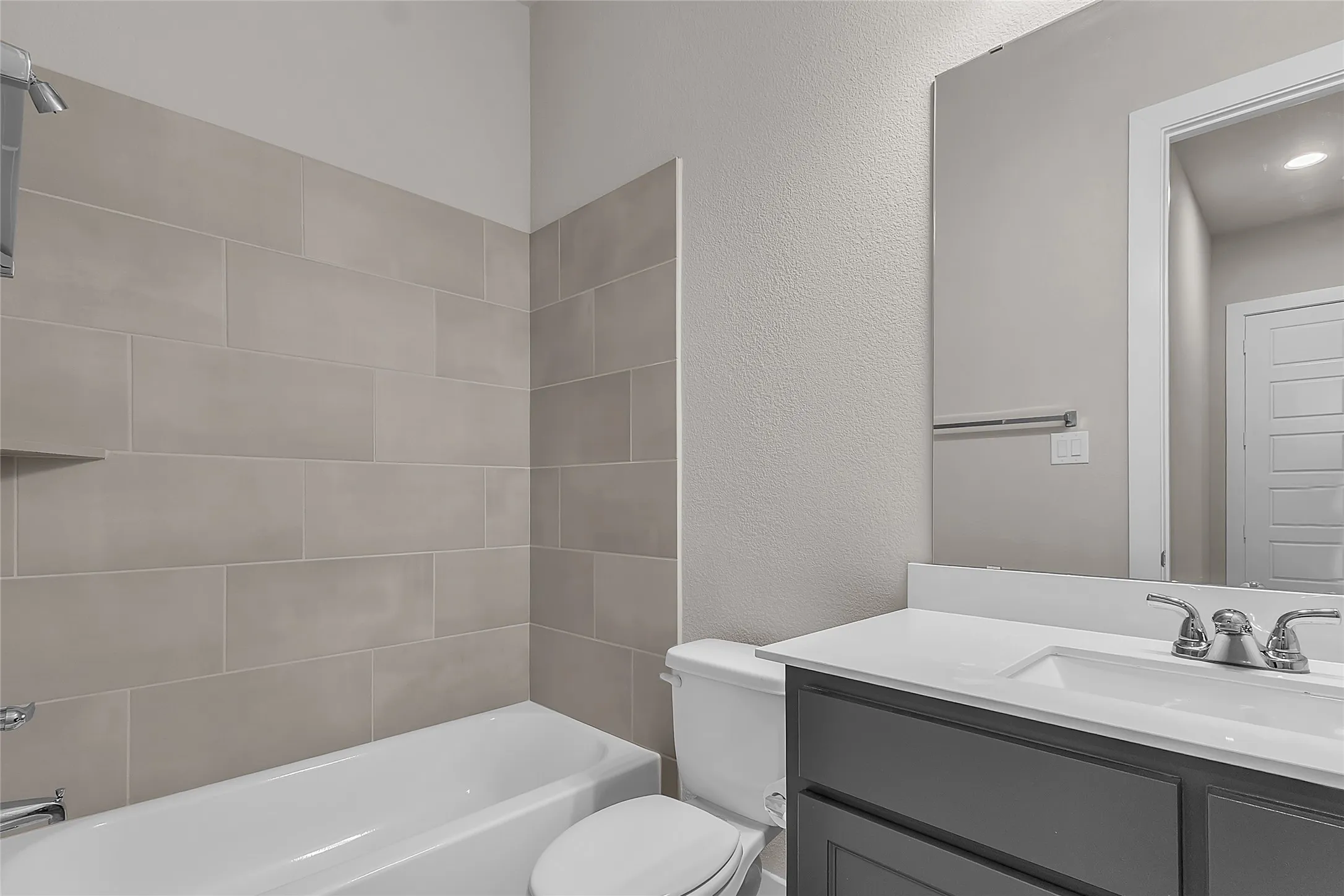 Bathroom with a tiled shower and tub combination, modern vanity with dual sinks, and soft gray wall finishes. Natural light from recessed lighting fixtures