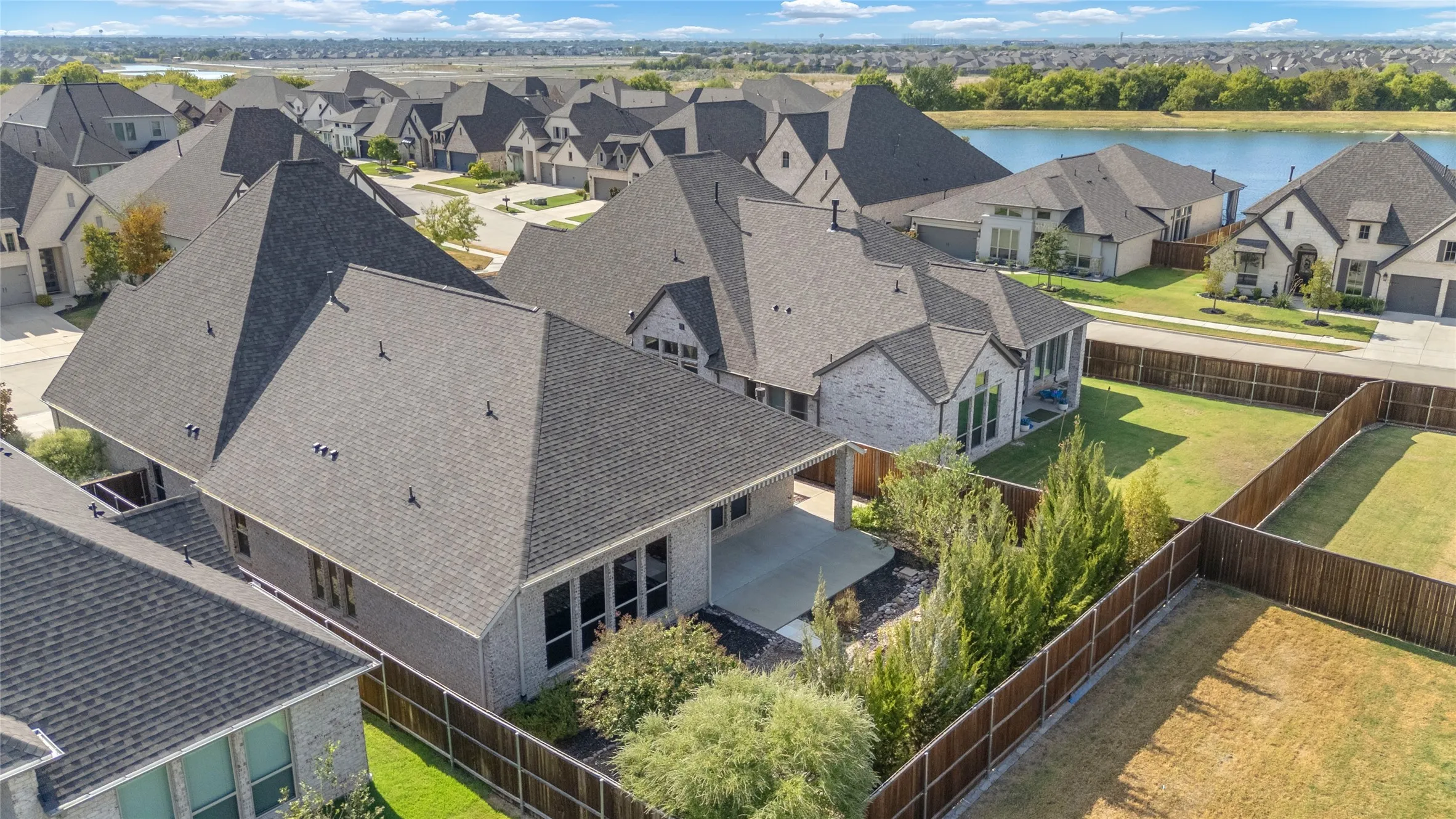 Aerial view of residential neighborhood with contemporary single-family homes, pitched roofs, and landscaped yards surrounding a calm lake.