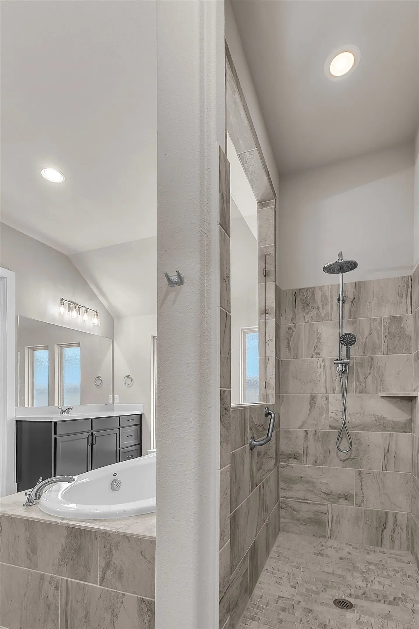 Luxurious bathroom with natural stone tile, double vanity, and walk-in shower featuring rainfall and handheld fixtures, complemented by recessed lighting