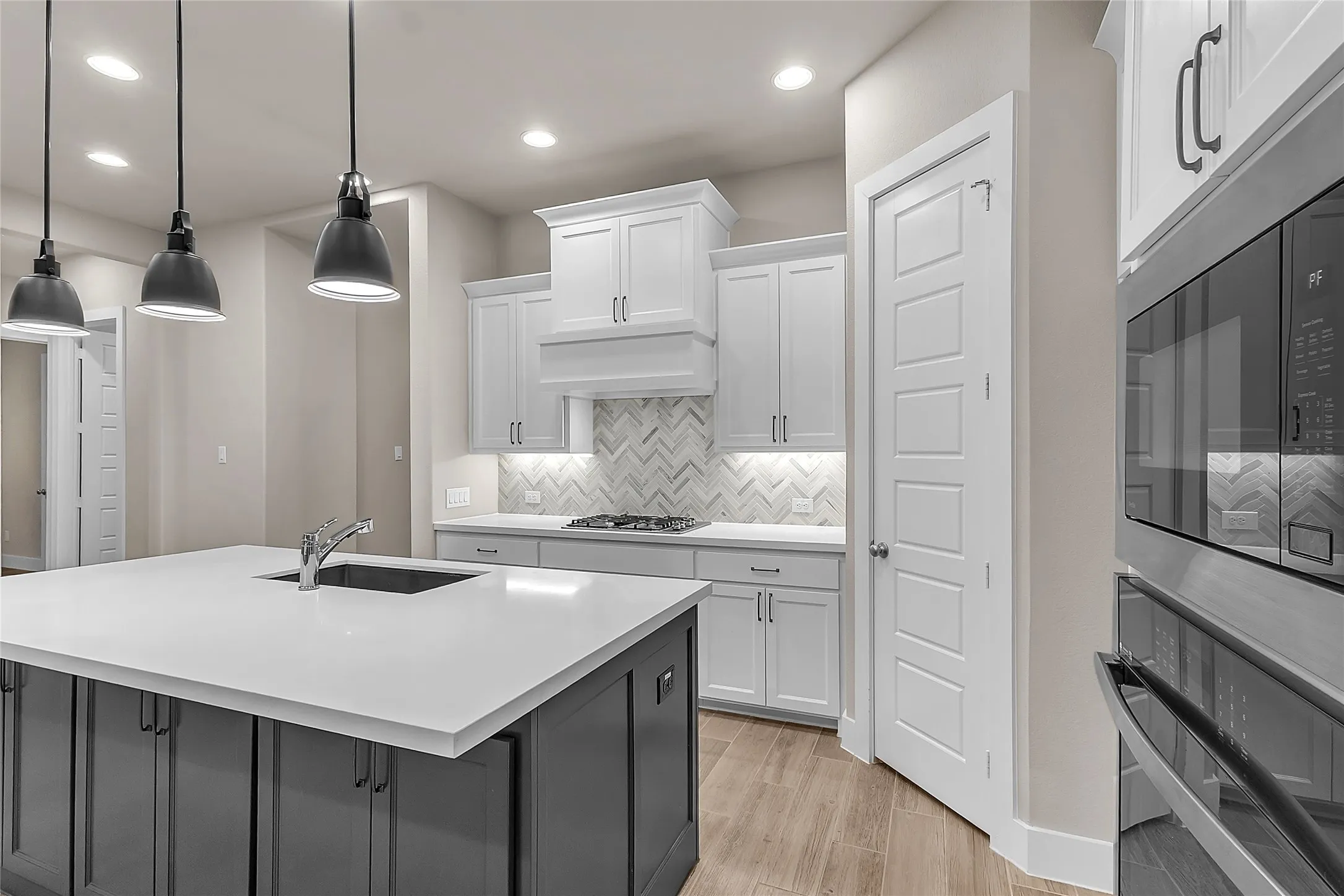 Open-plan kitchen with white cabinetry, quartz countertops, herringbone tile backsplash, stainless steel appliances, and pendant lighting over the island