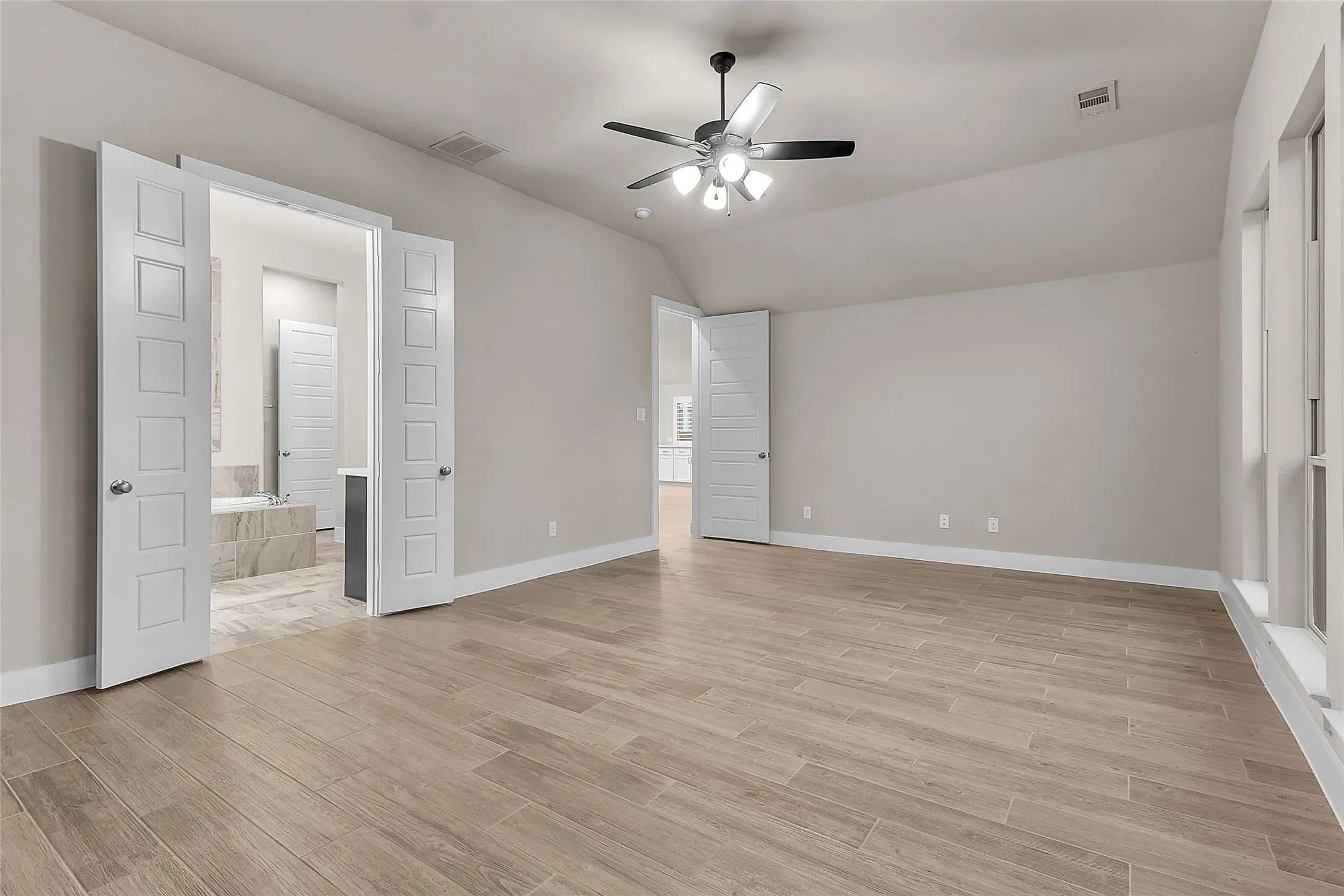 Primary bedroom with wood-look tile flooring, vaulted ceiling, ceiling fan, and access to an adjoining bathroom through double doors