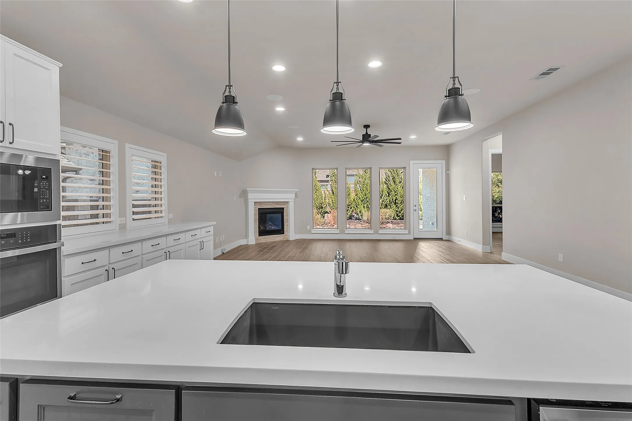 Open-plan living area with hardwood floors, recessed lighting, and large windows showcasing outdoor views and a central ceiling fan