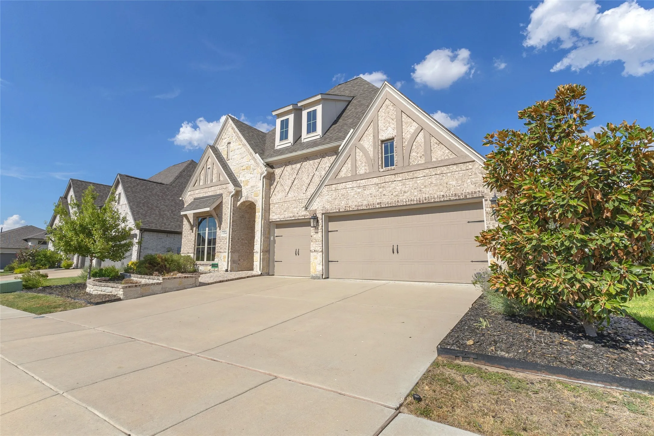 Three-car garage with smooth concrete driveway, stone accents, and large windows under a gabled roof with architectural shingles