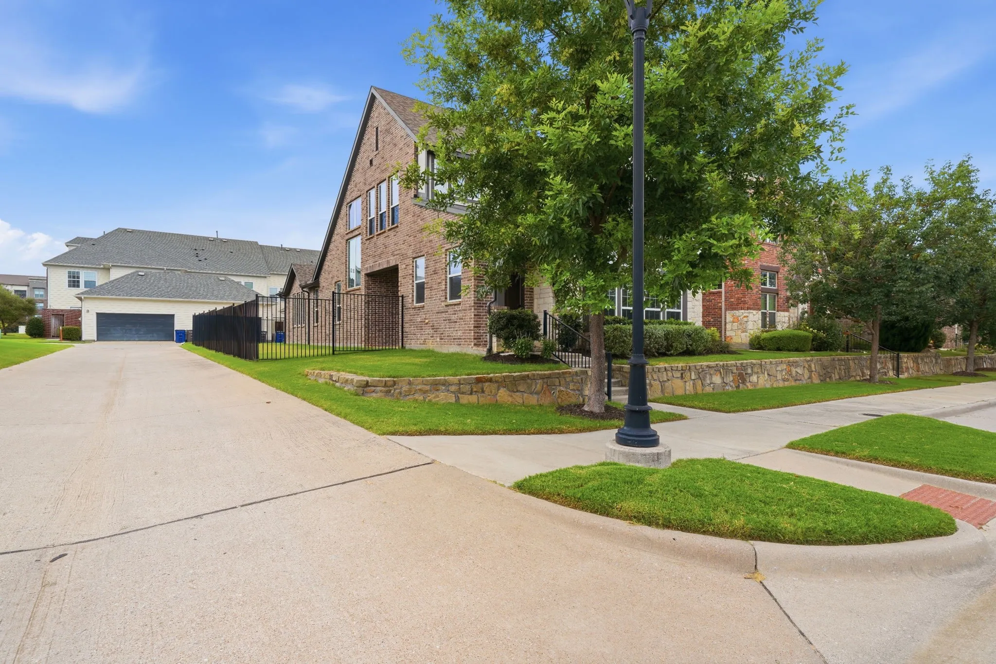 Brick exterior, gabled roofline, stone retaining wall, wrought iron fencing, concrete driveway