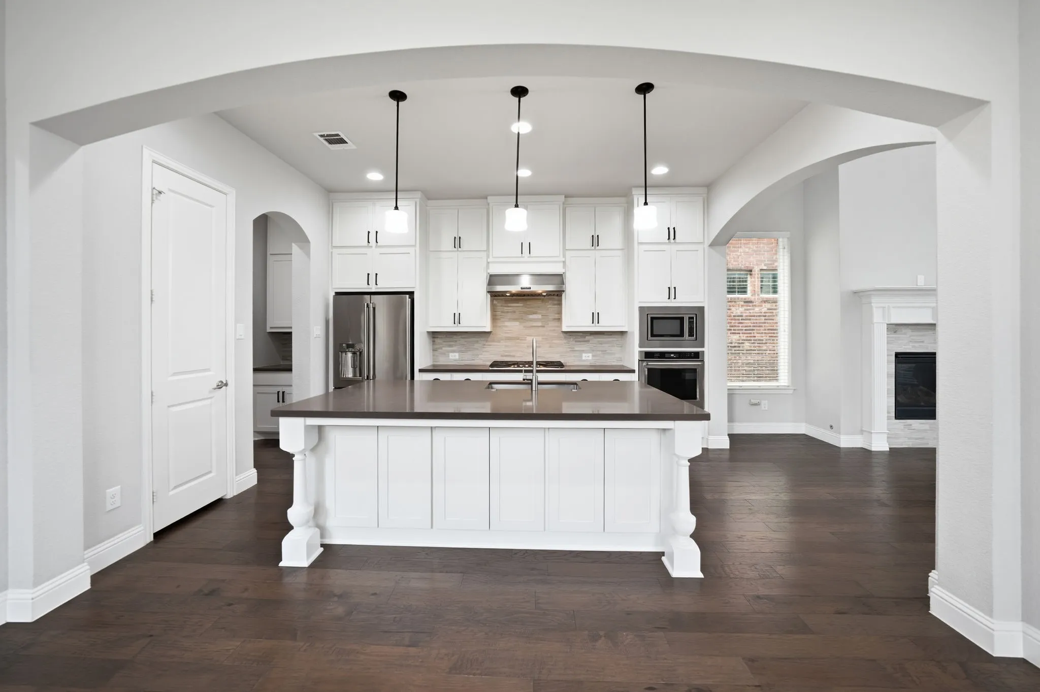 Kitchen featuring an island with pendant lighting, stainless steel appliances, white cabinetry, and wood-finish flooring