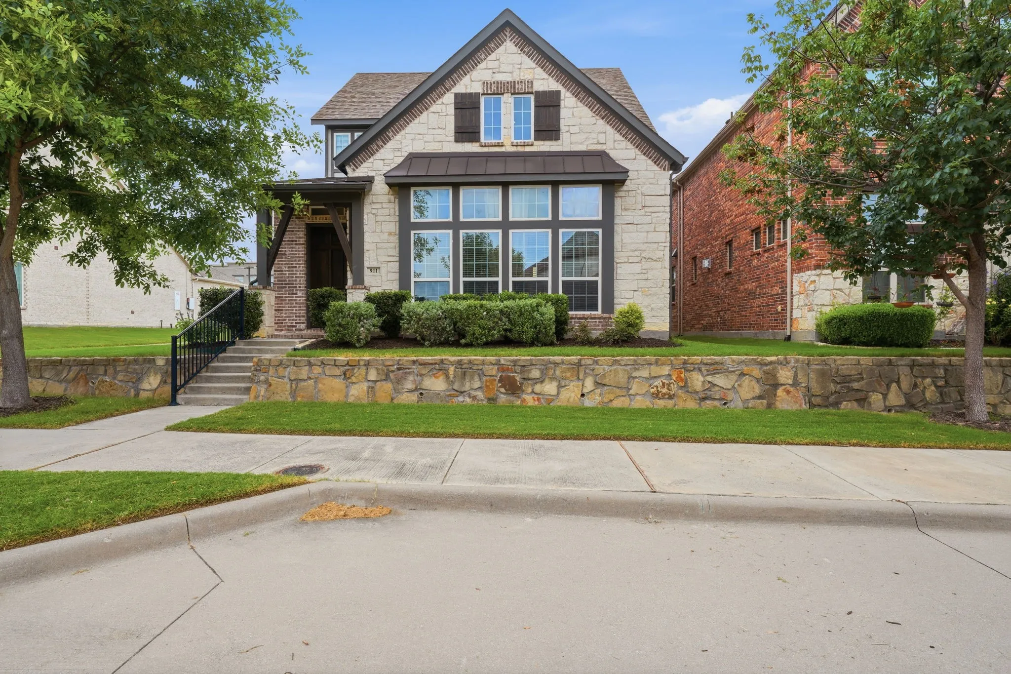 Stone and brick exterior with dark trim and shutters, prominent bay window, covered entry, and tiered front landscaping