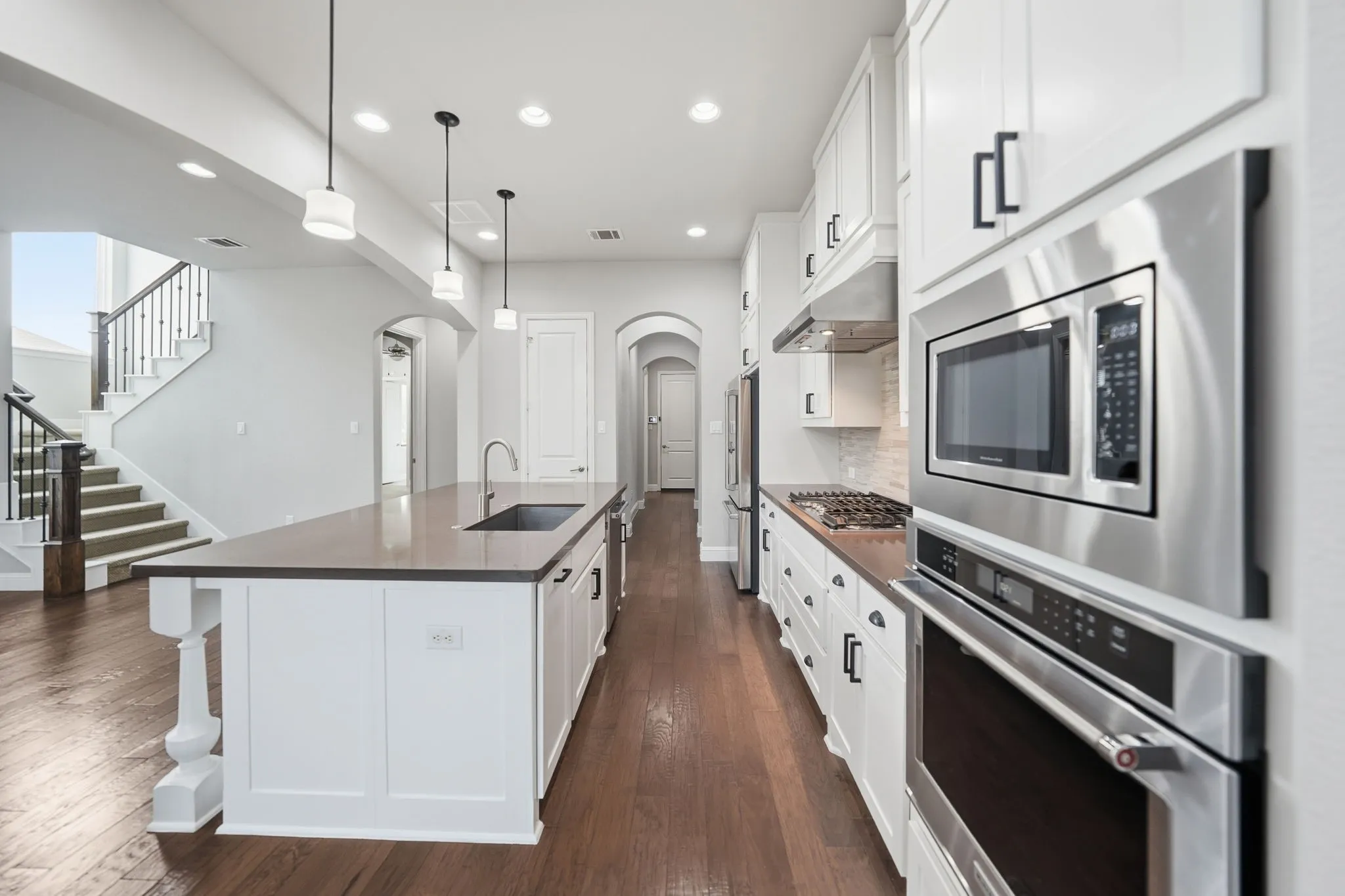 Gourmet kitchen with stainless steel appliances, dark wood-finish flooring, recessed lighting, white cabinetry, and an expansive island featuring a built-in sink and pendant lighting