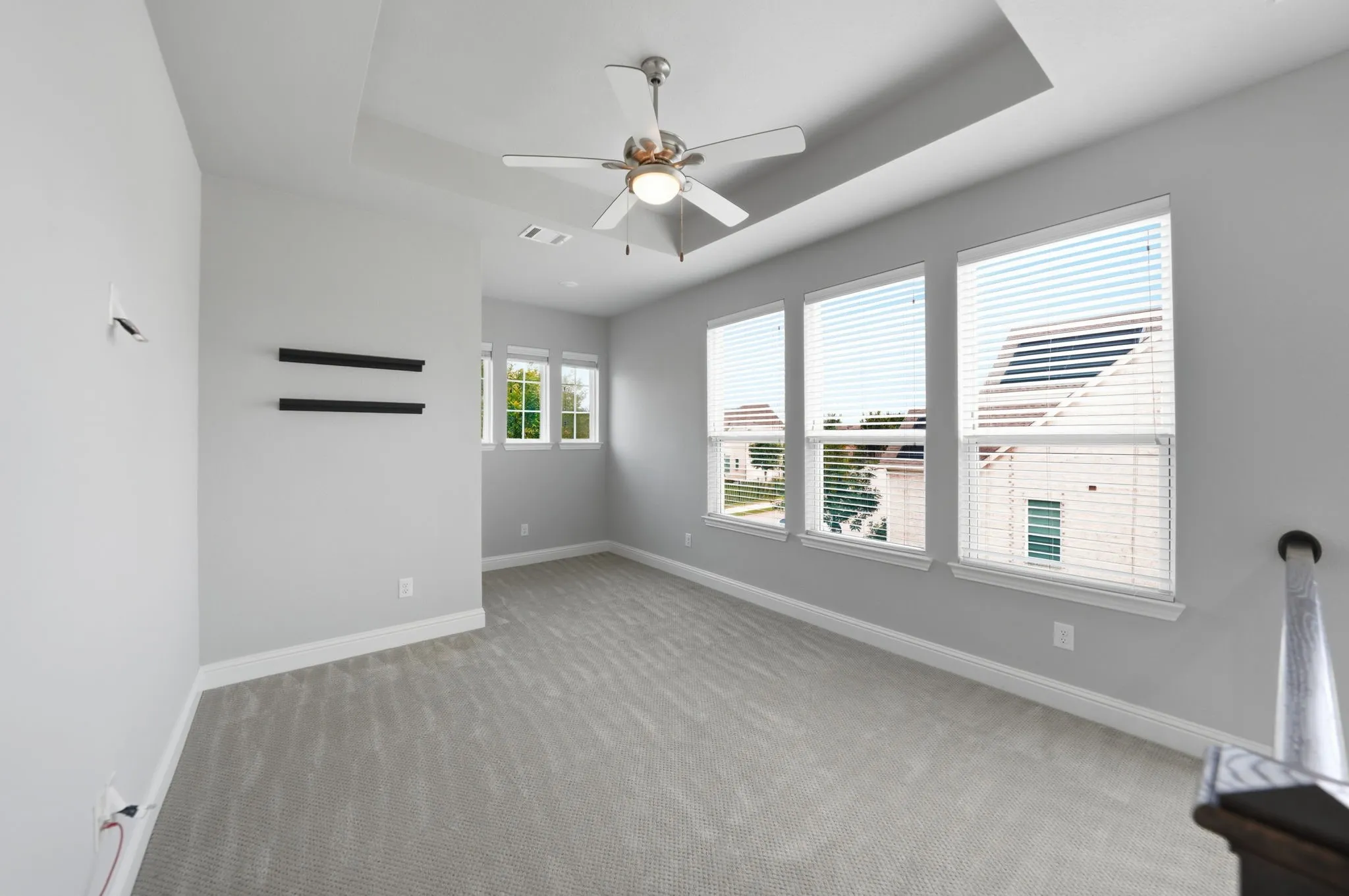 Tray ceiling, flush-mount ceiling fan, multiple windows with blinds, gray carpeting, and white baseboards