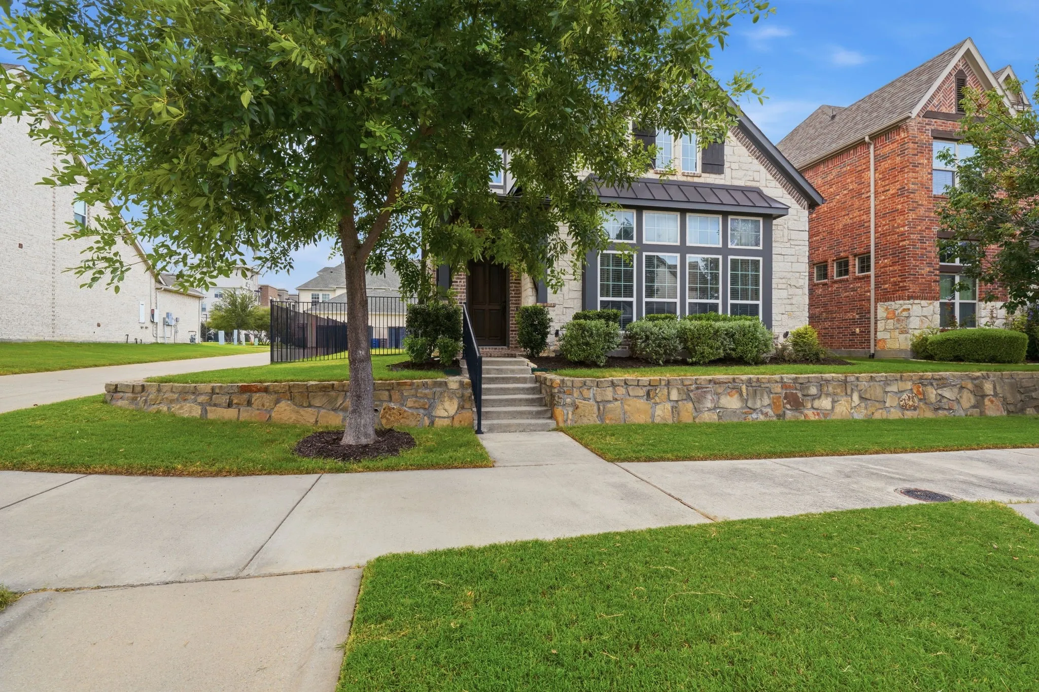 Stone and brick facade with a bay window, a manicured lawn, and a stone retaining wall
