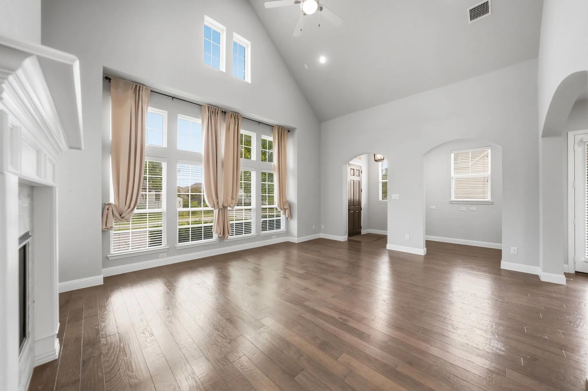 Vaulted ceiling with a ceiling fan, wood-finish flooring, white fireplace mantel, and large picture windows