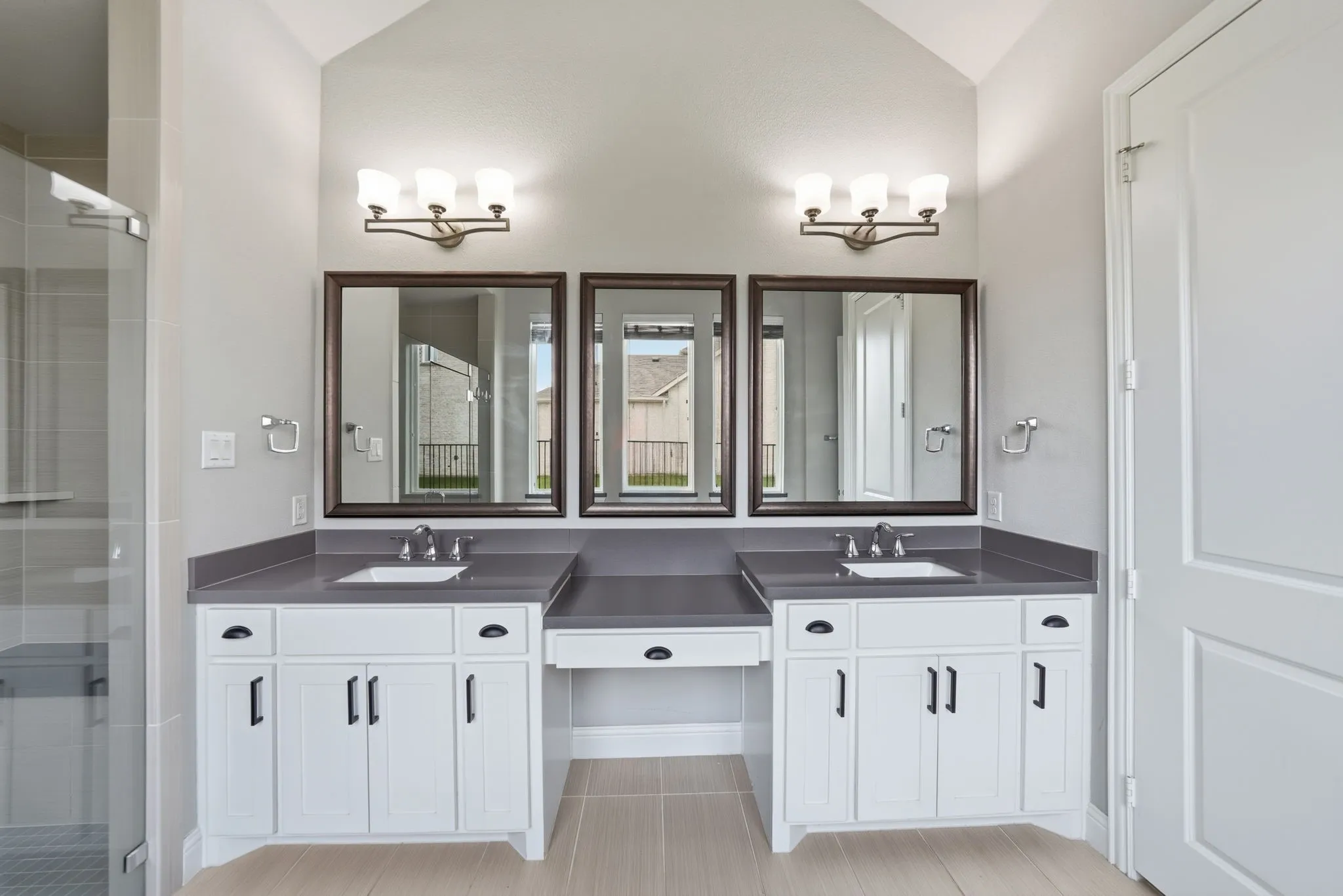 Dual vanities with undermount sinks, flanked by white cabinetry and dark countertops