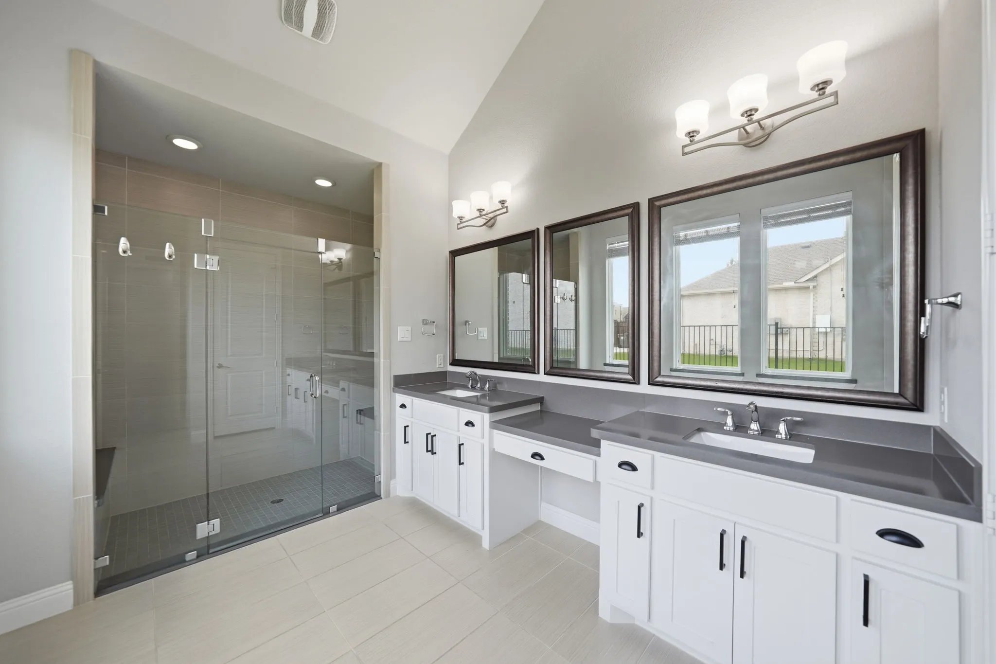 Spacious bathroom featuring a large glass-enclosed shower, dual vanity with solid surface countertops, white cabinetry with dark hardware, and tiled flooring