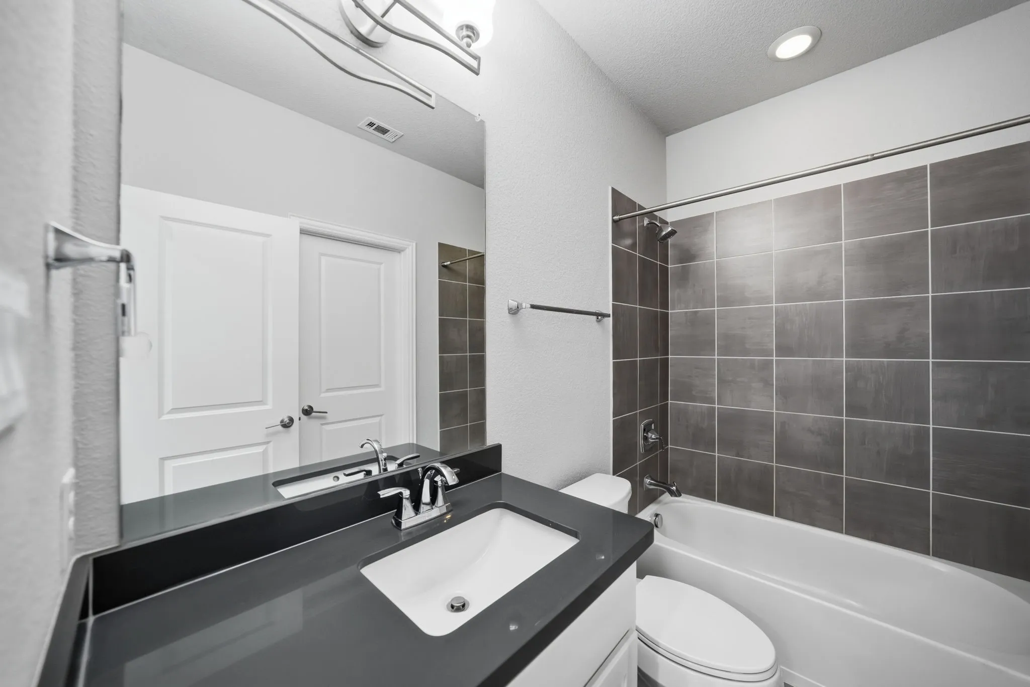 White drop-in sink, dark countertop, chrome fixtures, built-in tub with tile surround, and recessed lighting