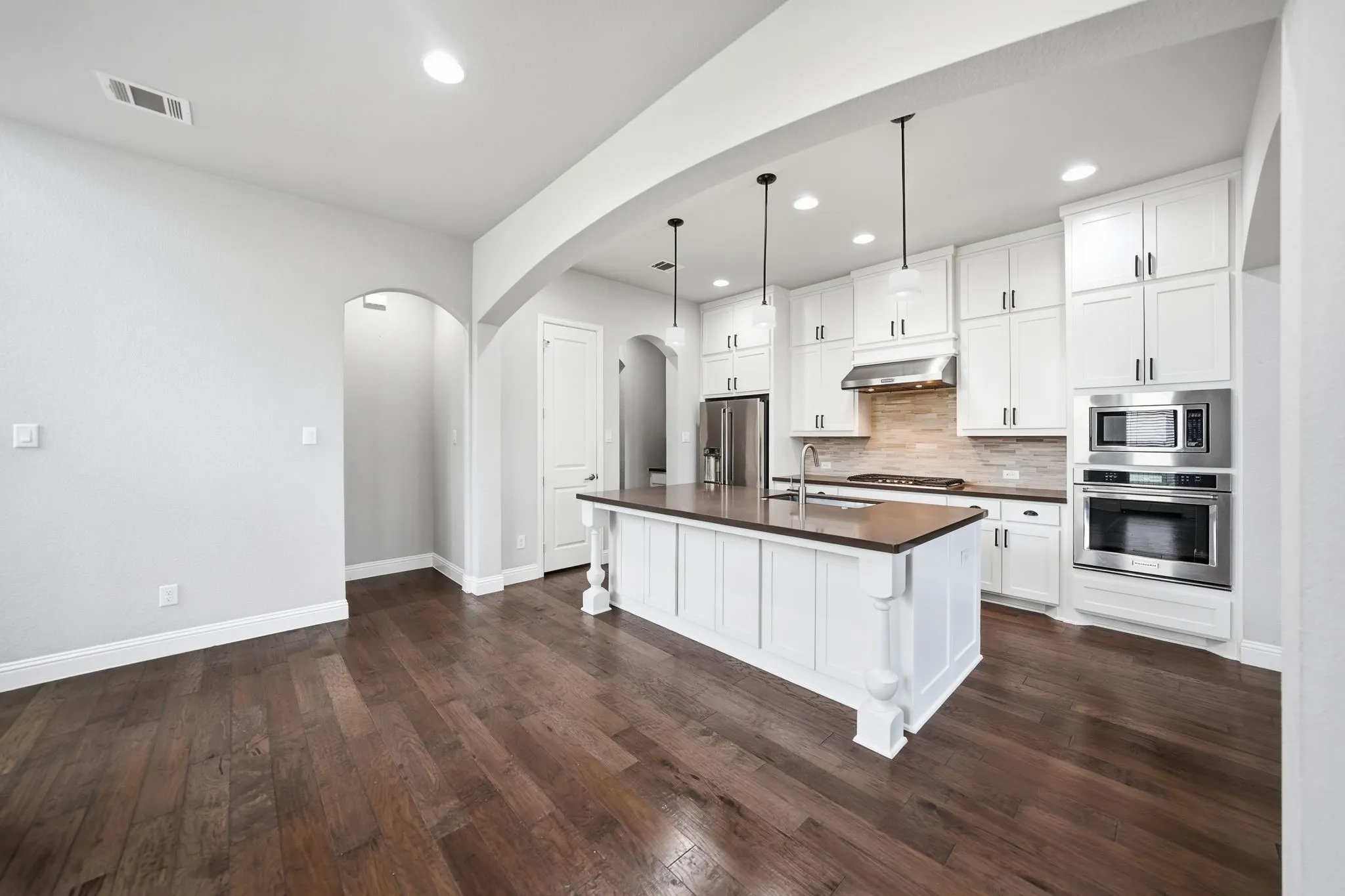 Wood-finish flooring throughout, white shaker cabinetry, stainless steel appliances, kitchen island with built-in sink, and recessed lighting