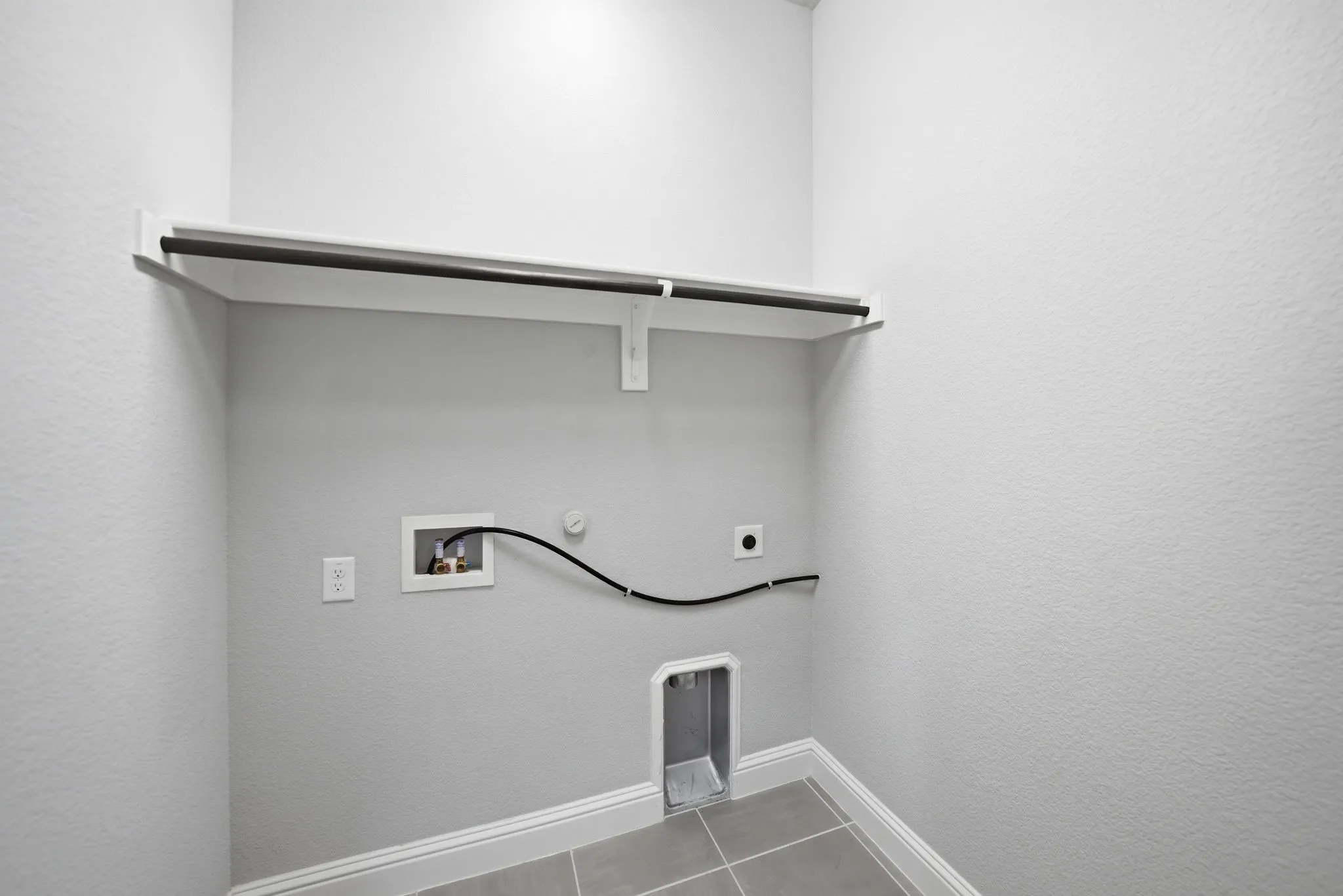 Laundry area featuring a built-in shelf with hanging rod, durable tile flooring, and utility hookups