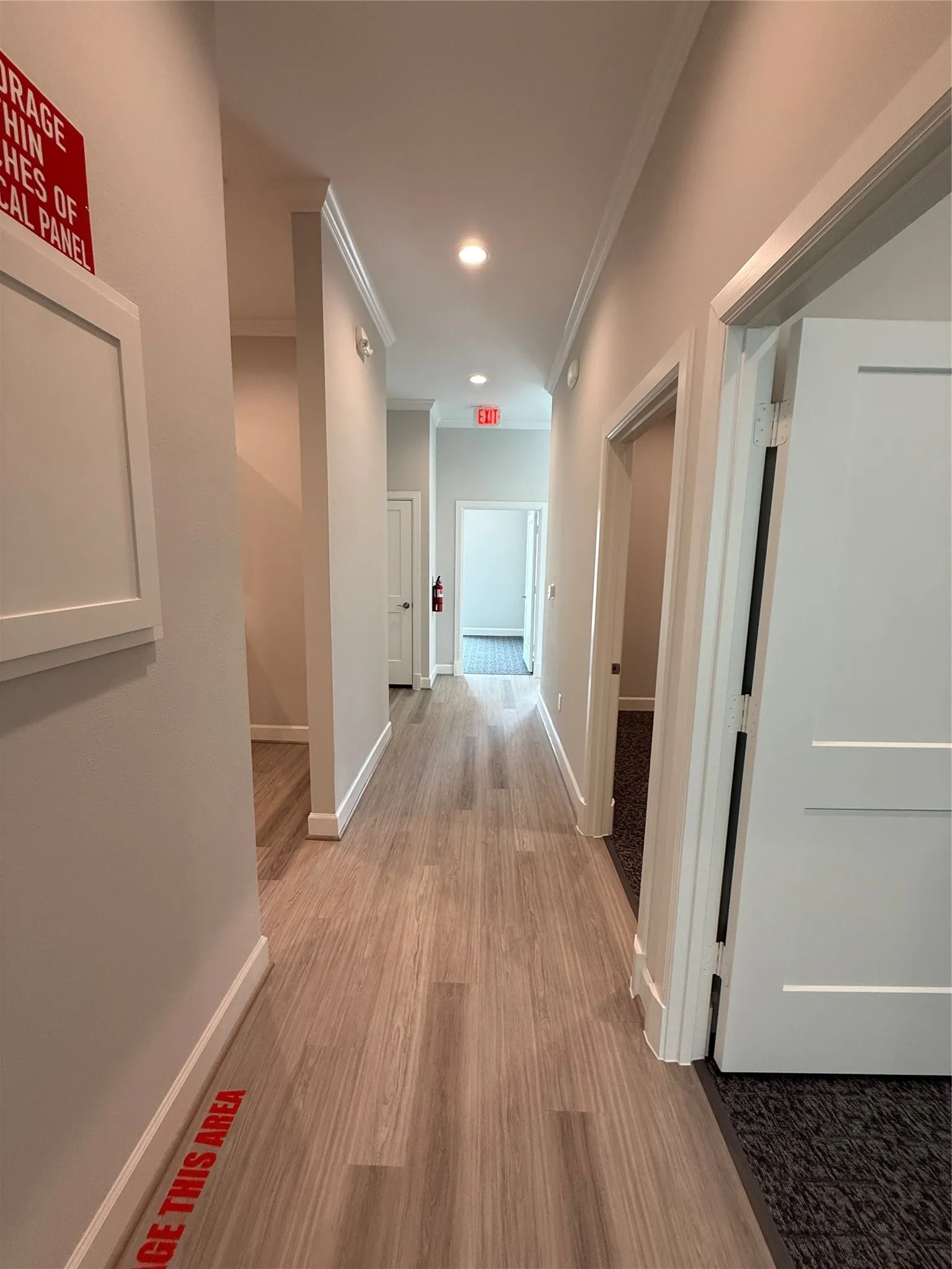 Recessed lighting illuminates a hallway with wood-finish flooring and crown molding