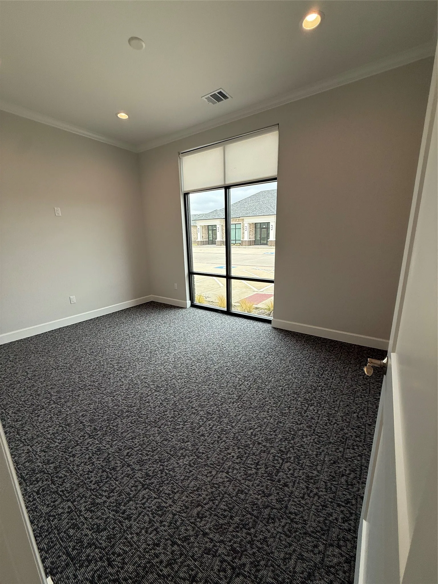 Spacious room featuring textured carpeting, full-height window with roller shade, recessed lighting, and crown molding