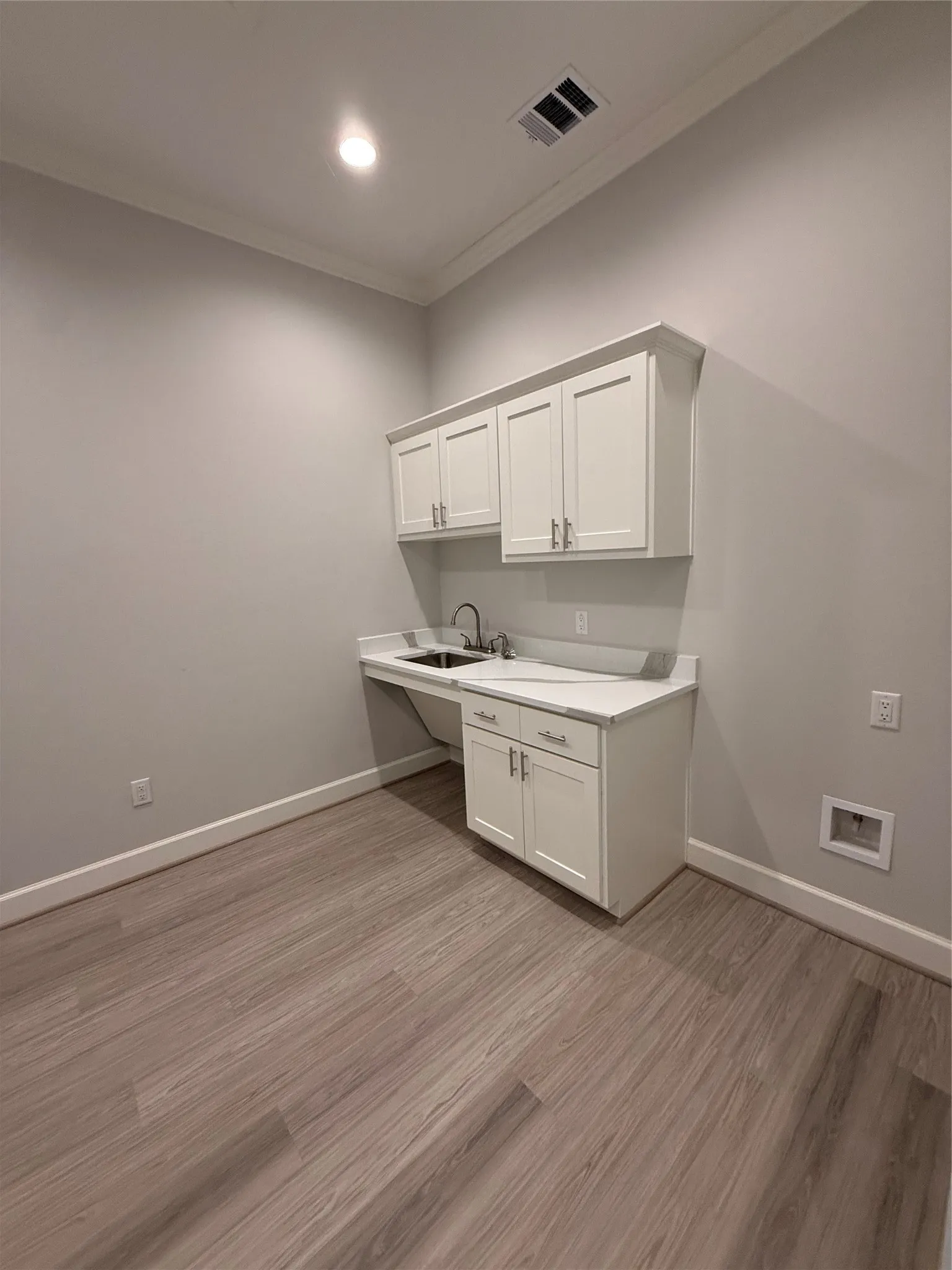 White shaker cabinetry with brushed nickel hardware, undermount sink, light-toned countertop, wood-finish flooring, and crown molding