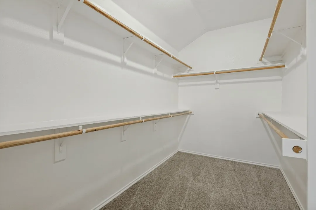 Carpeted walk-in closet with multiple white shelving units and wooden rods