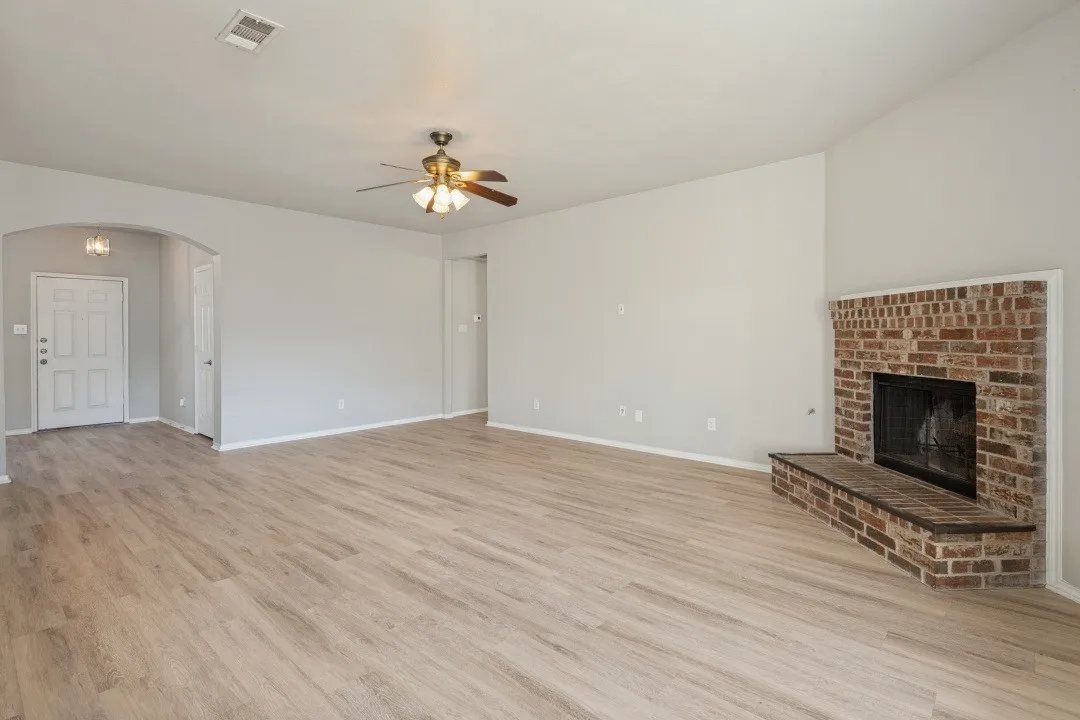 Light wood-finish flooring, a brick fireplace, a vaulted ceiling, and an arched entryway
