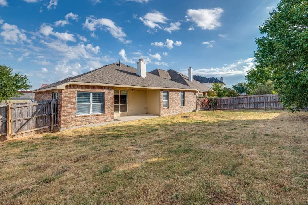 Expansive backyard with a wood privacy fence, brick exterior, and a covered patio