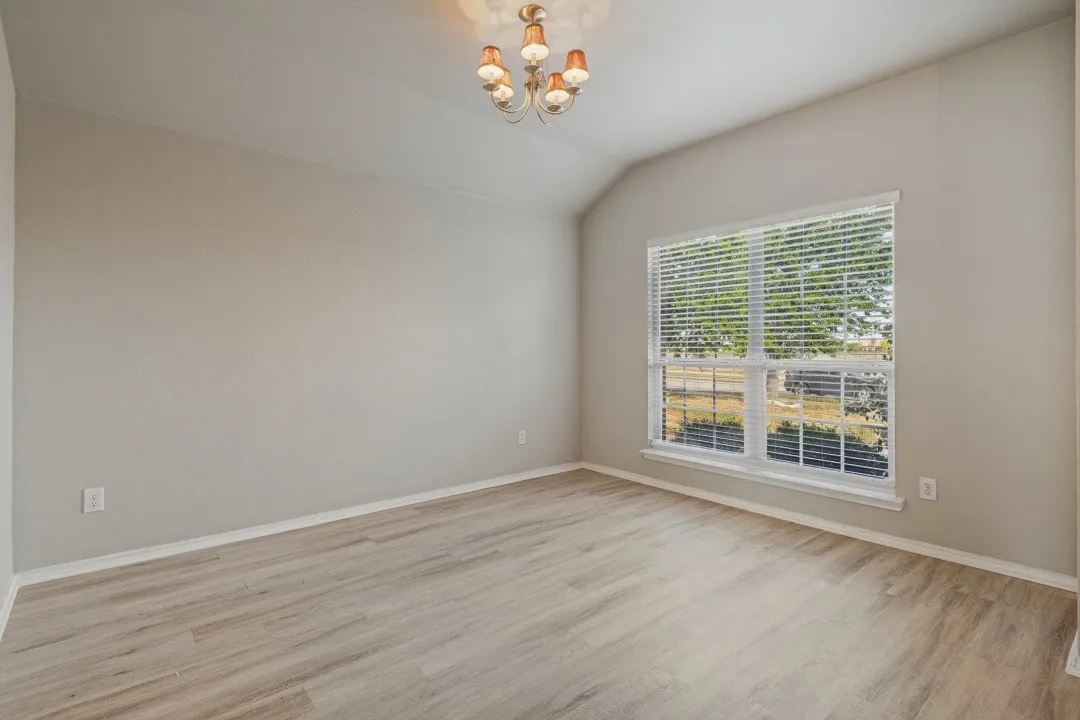 Vaulted ceiling, wood-finish flooring, large window with blinds, and ceiling-mounted light fixture
